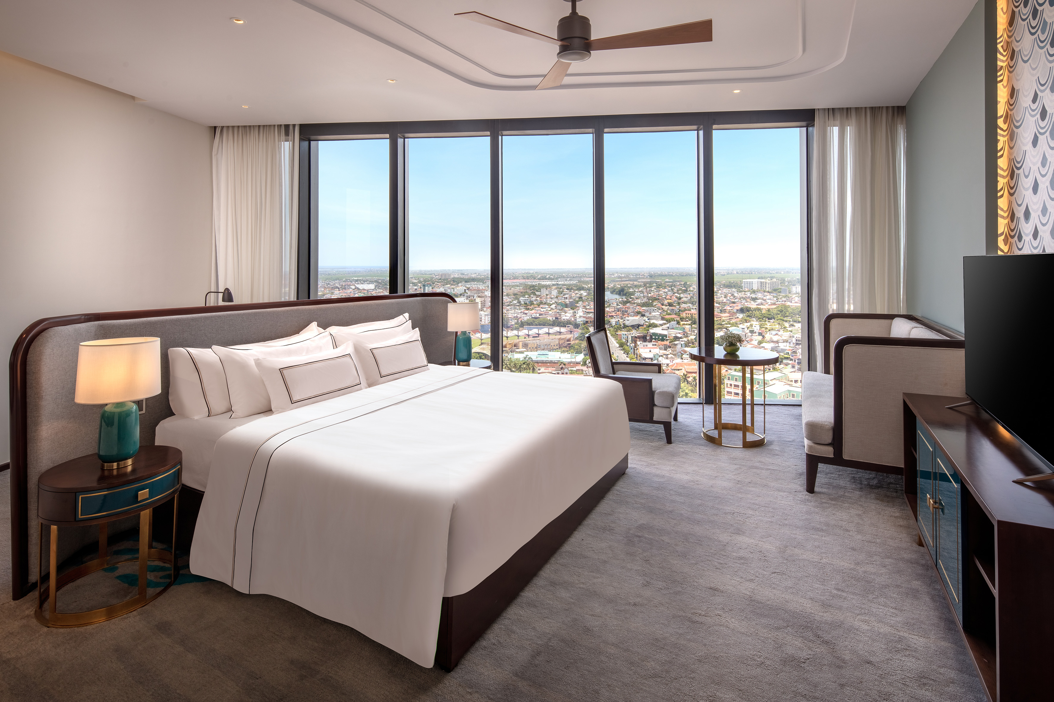 Luxury hotel room with city view, large bed, modern decor, and ceiling fan.