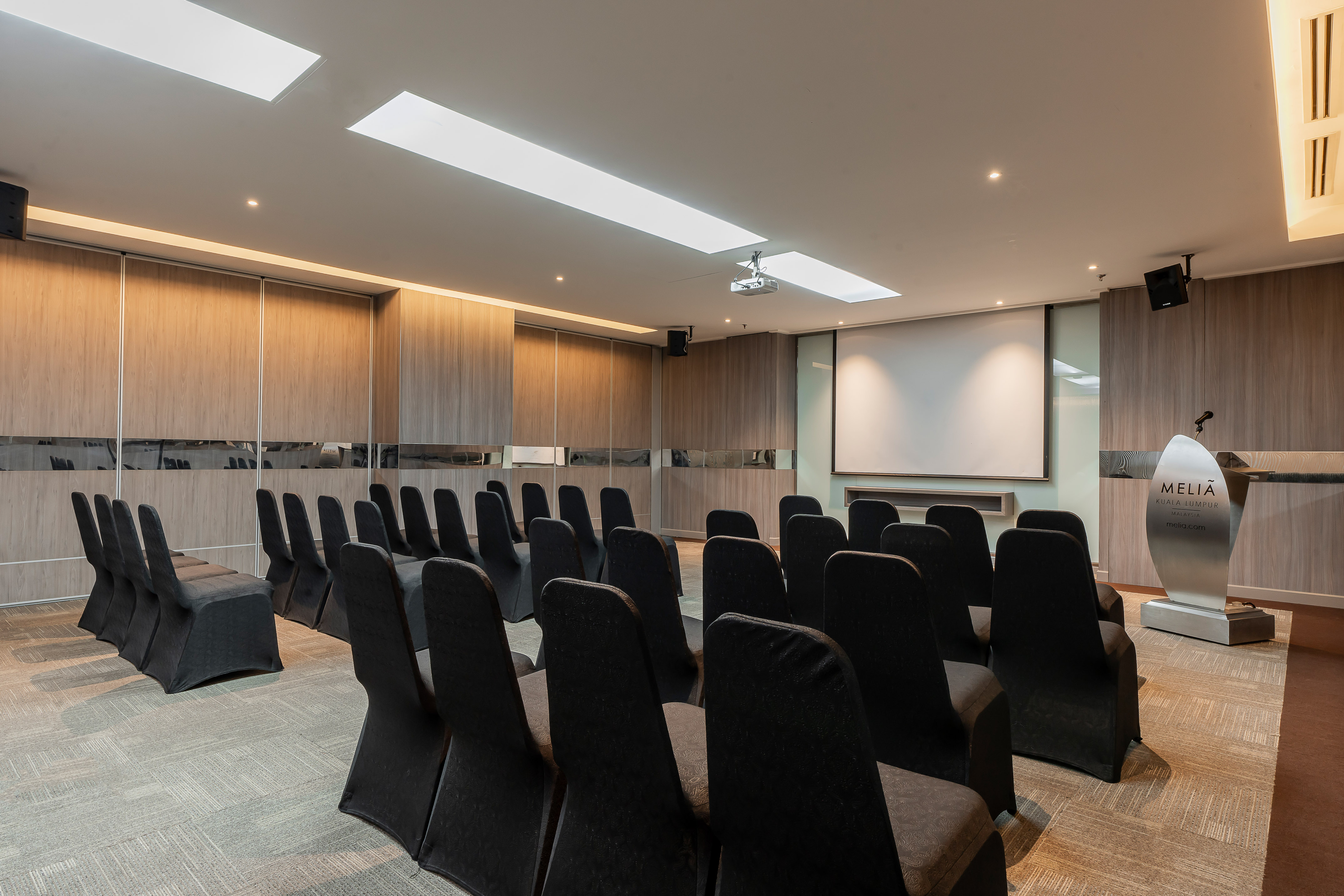 Meliá Kuala Lumpur conference room with projector screen, podium, and seating.