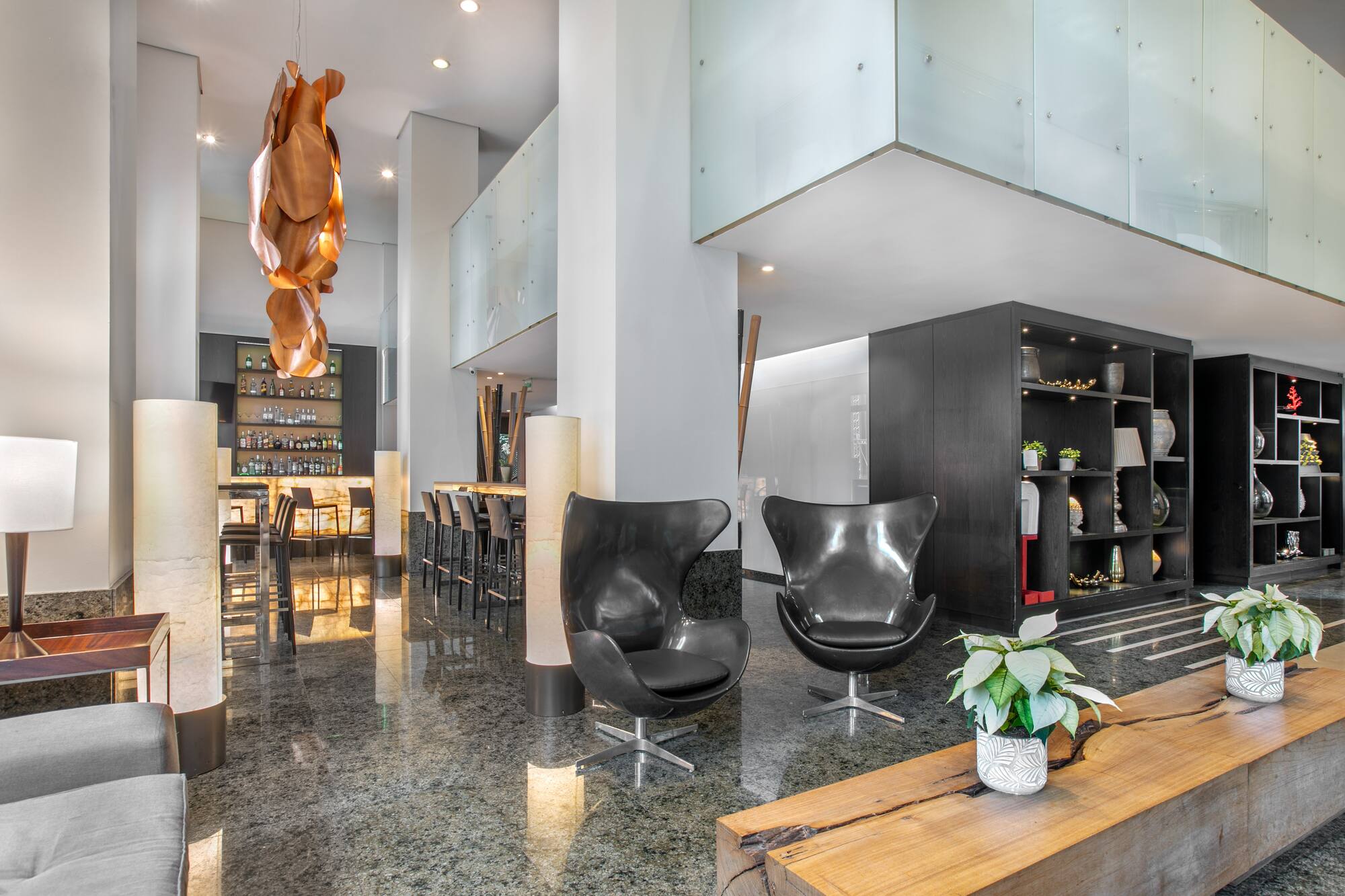 Modern hotel lobby lounge with sleek bar, black egg chairs, granite floor.