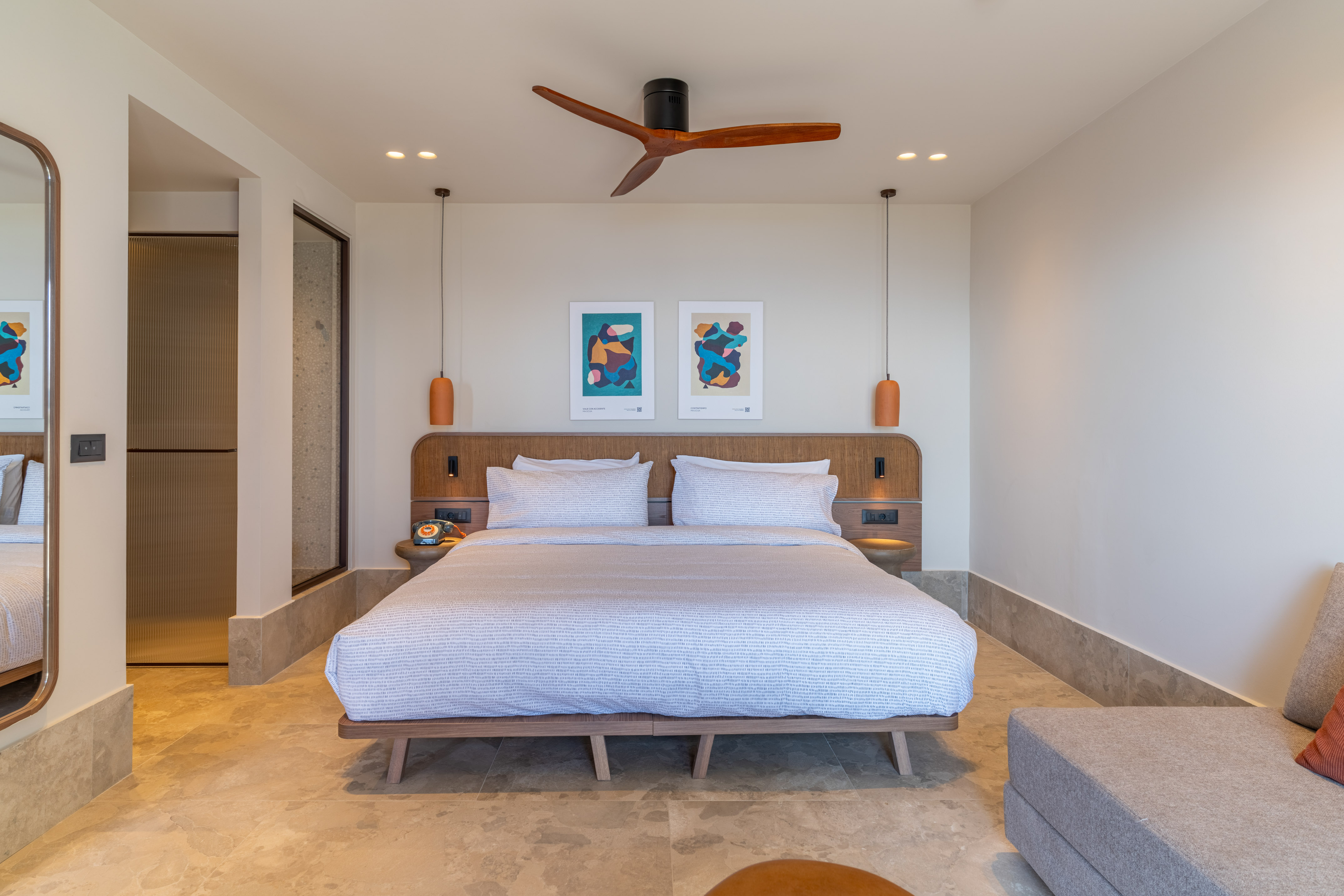 Modern hotel bedroom with wooden bed, abstract art, ceiling fan, and stone floor.