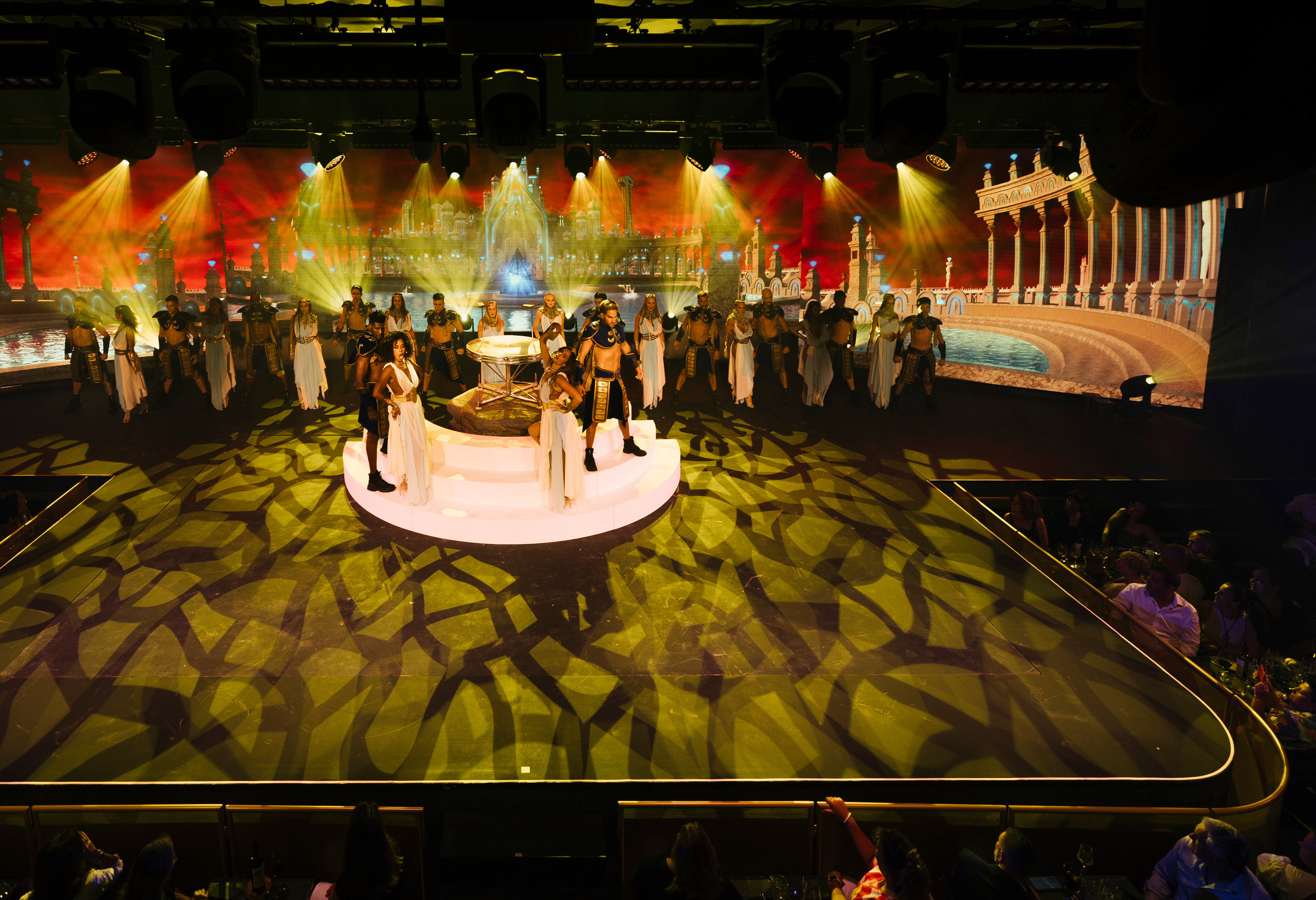 Live stage show with performers in ancient costumes, elaborate city backdrop.