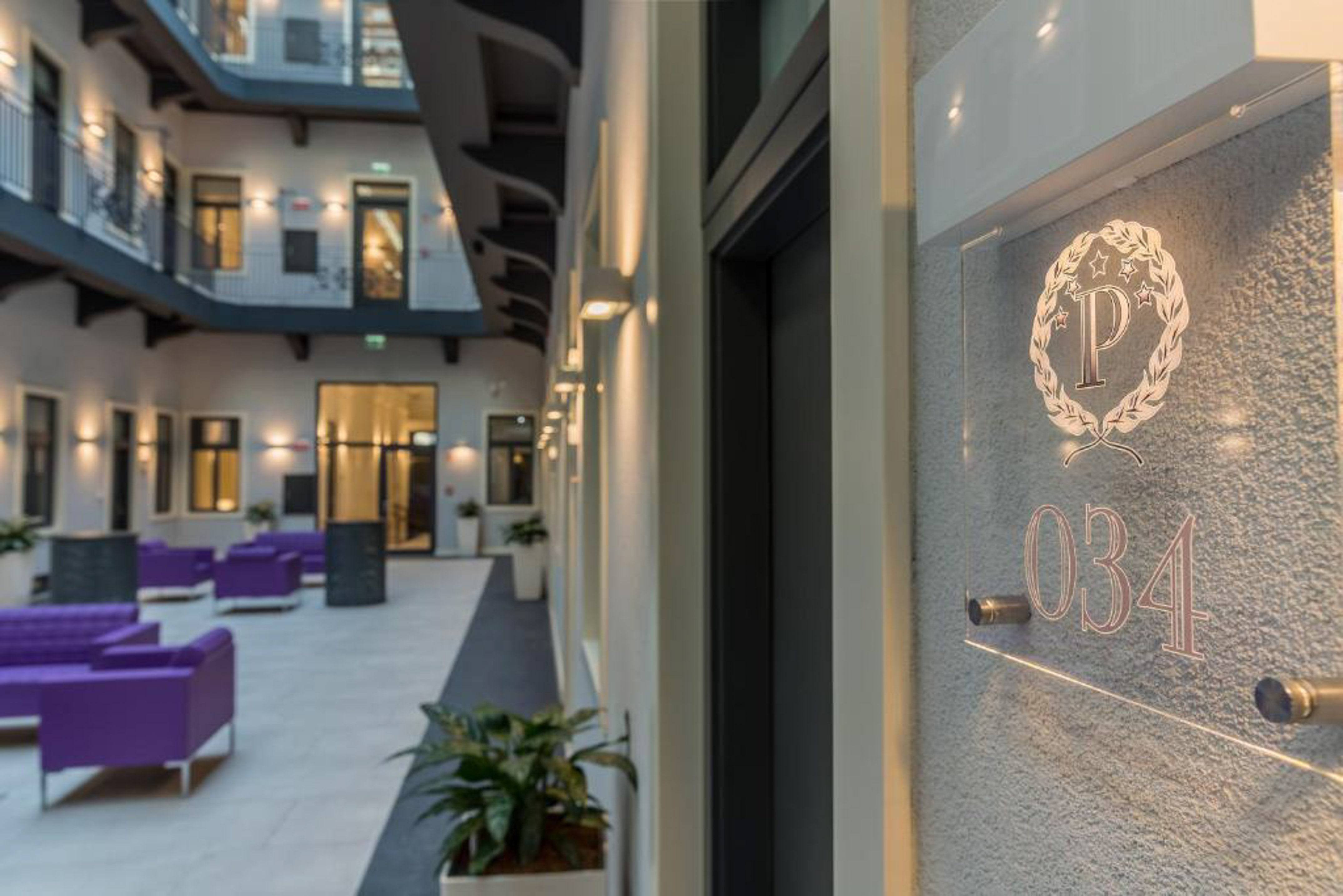 Modern hotel atrium with purple lounge seating, balconies, and room 034 sign.
