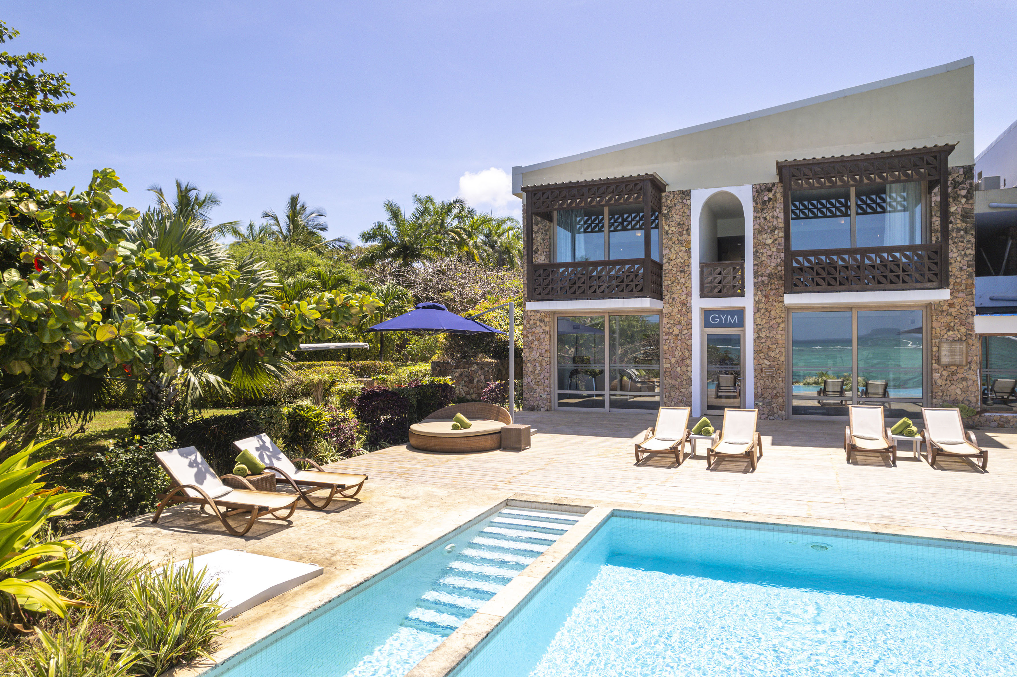 Luxury tropical villa with swimming pool, deck, sun loungers, and lush garden.