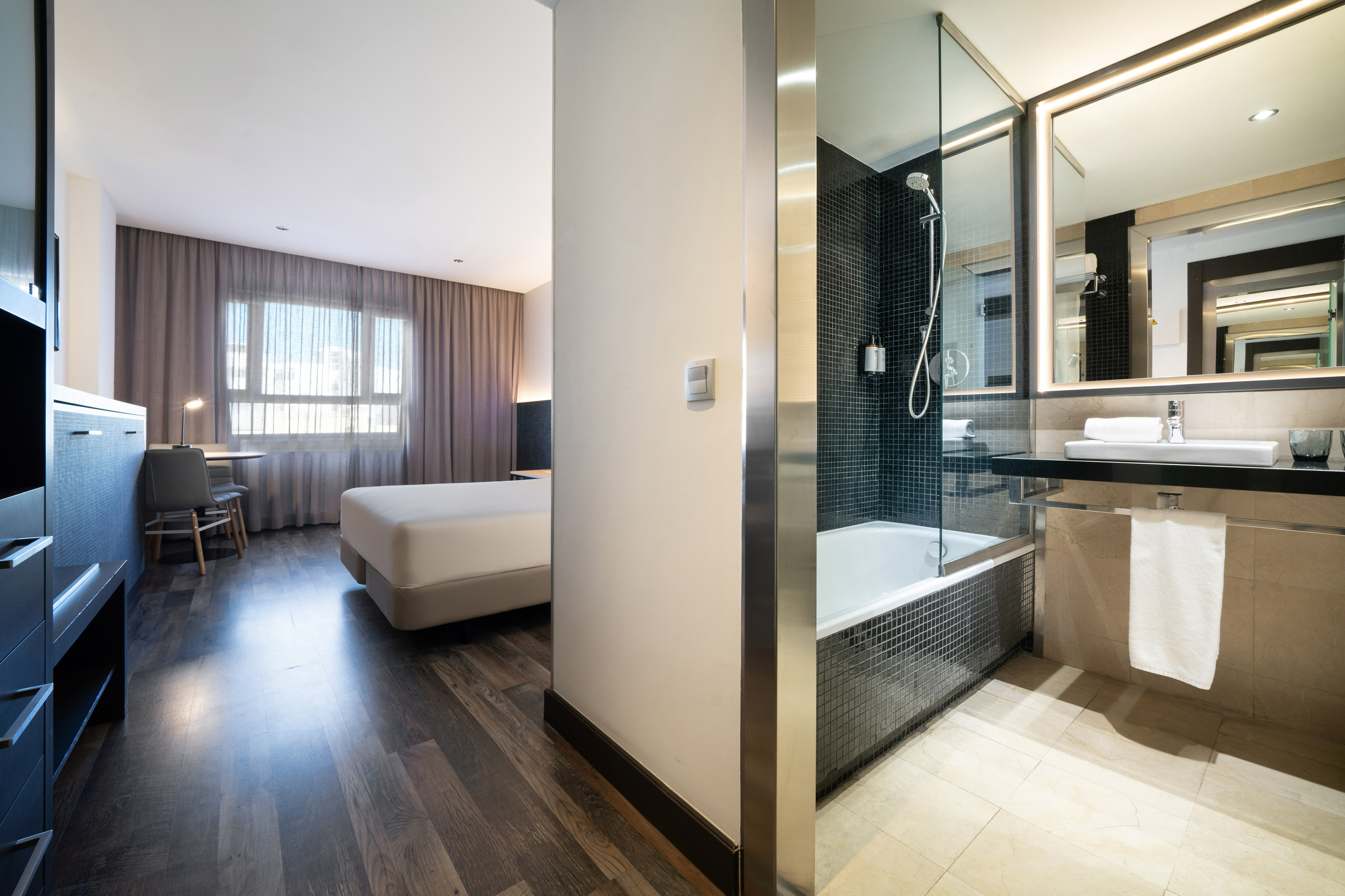 Modern hotel room and bathroom featuring a bed, desk, shower, and bathtub.