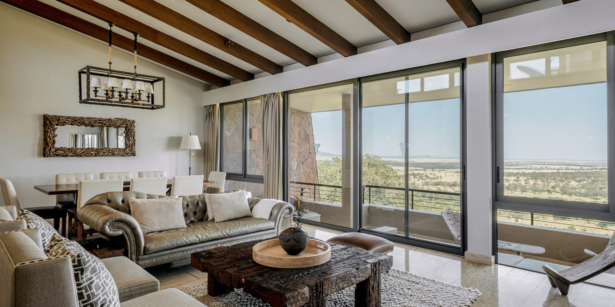Safari lodge living room with savanna views, rustic wooden decor, and large windows.