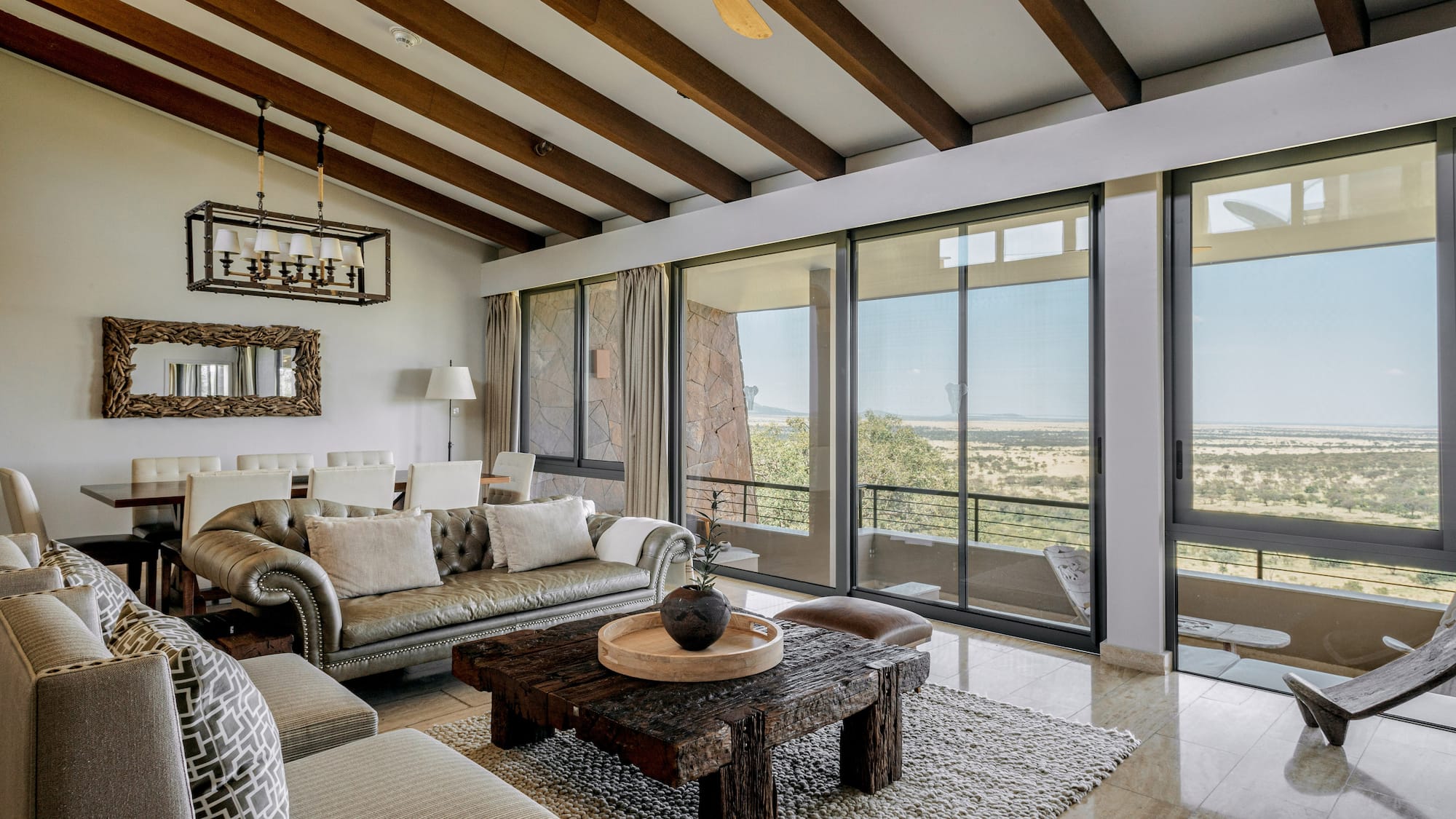 Safari lodge living room with savanna views, rustic wooden decor, and large windows.