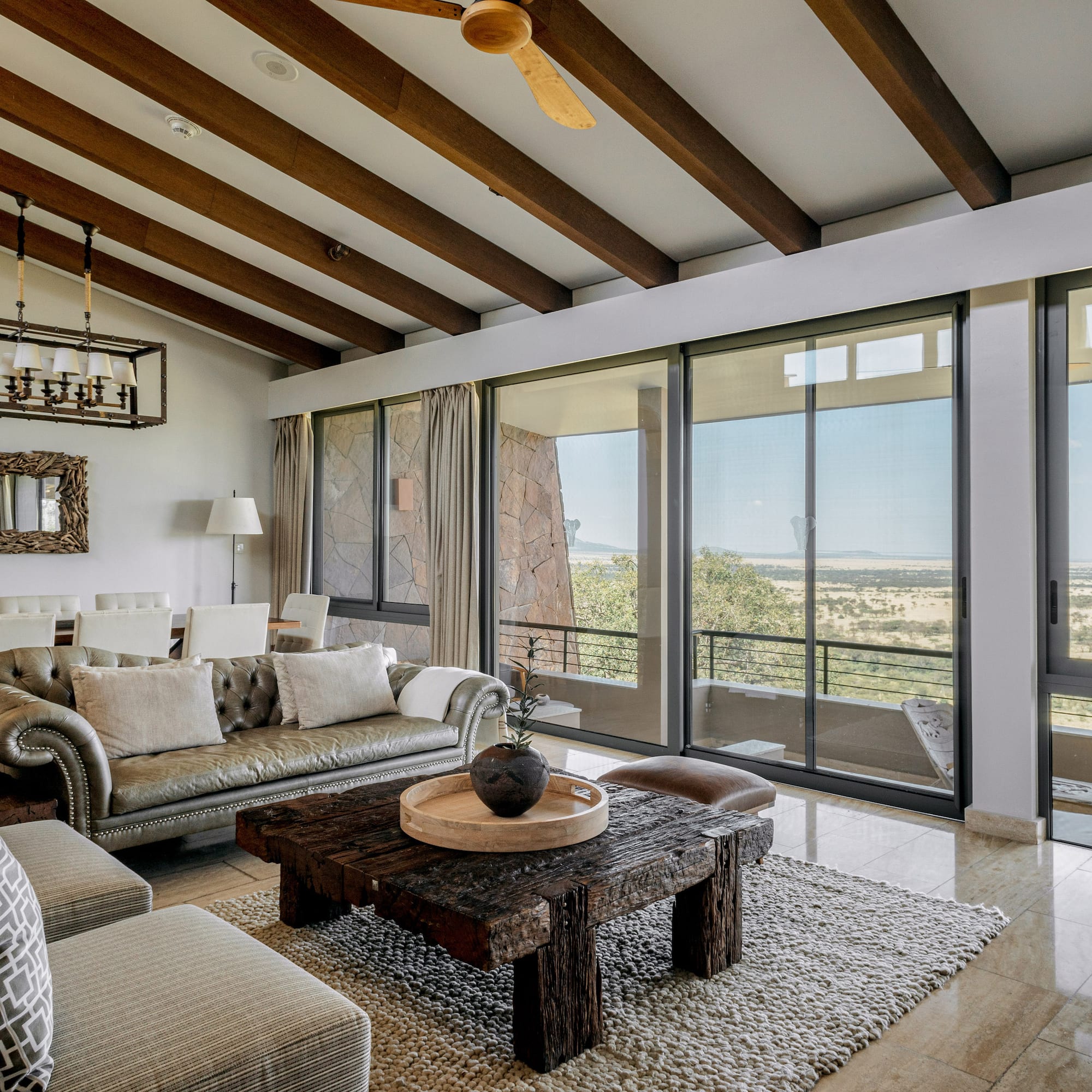 Safari lodge living room with savanna views, rustic wooden decor, and large windows.