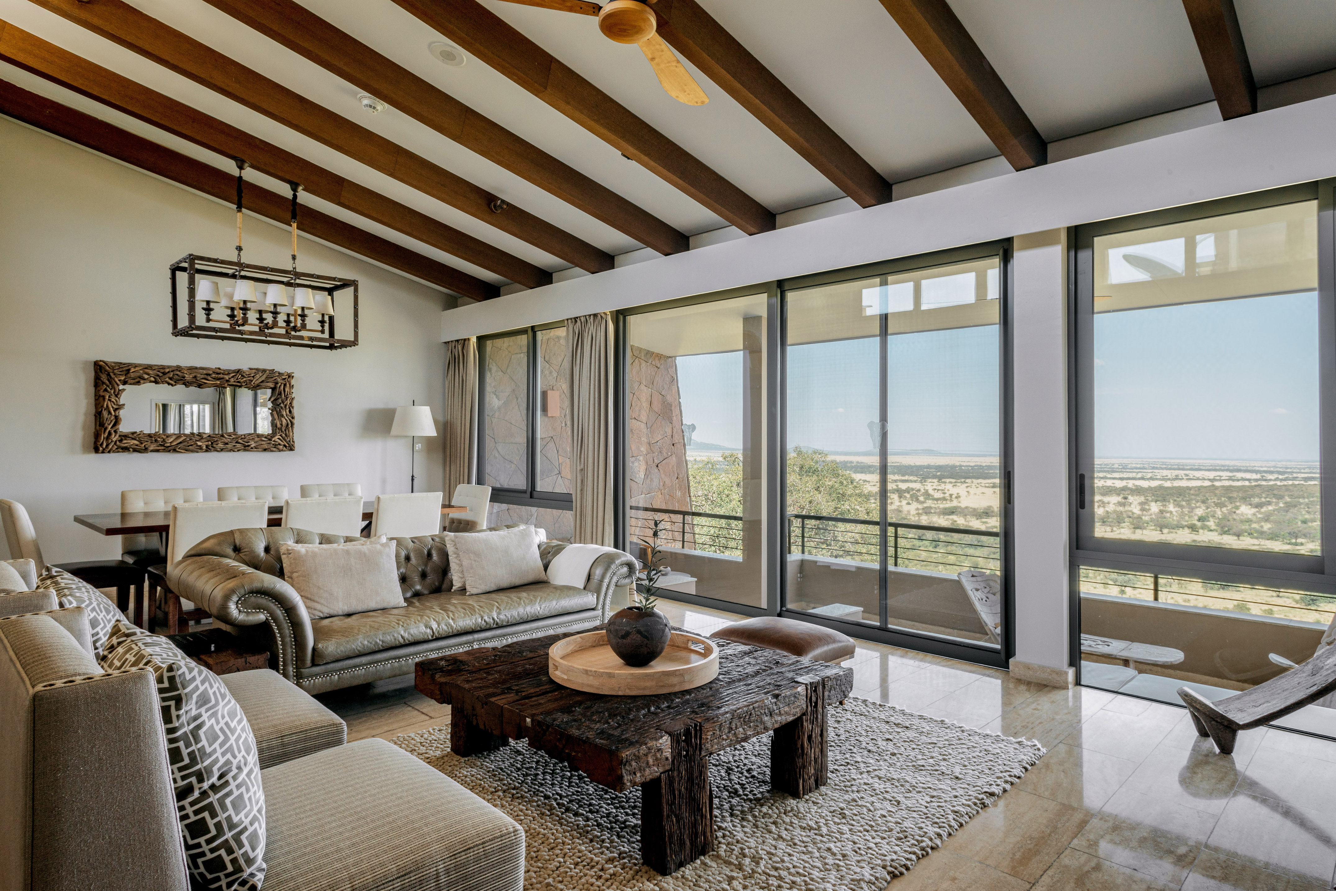 Safari lodge living room with savanna views, rustic wooden decor, and large windows.
