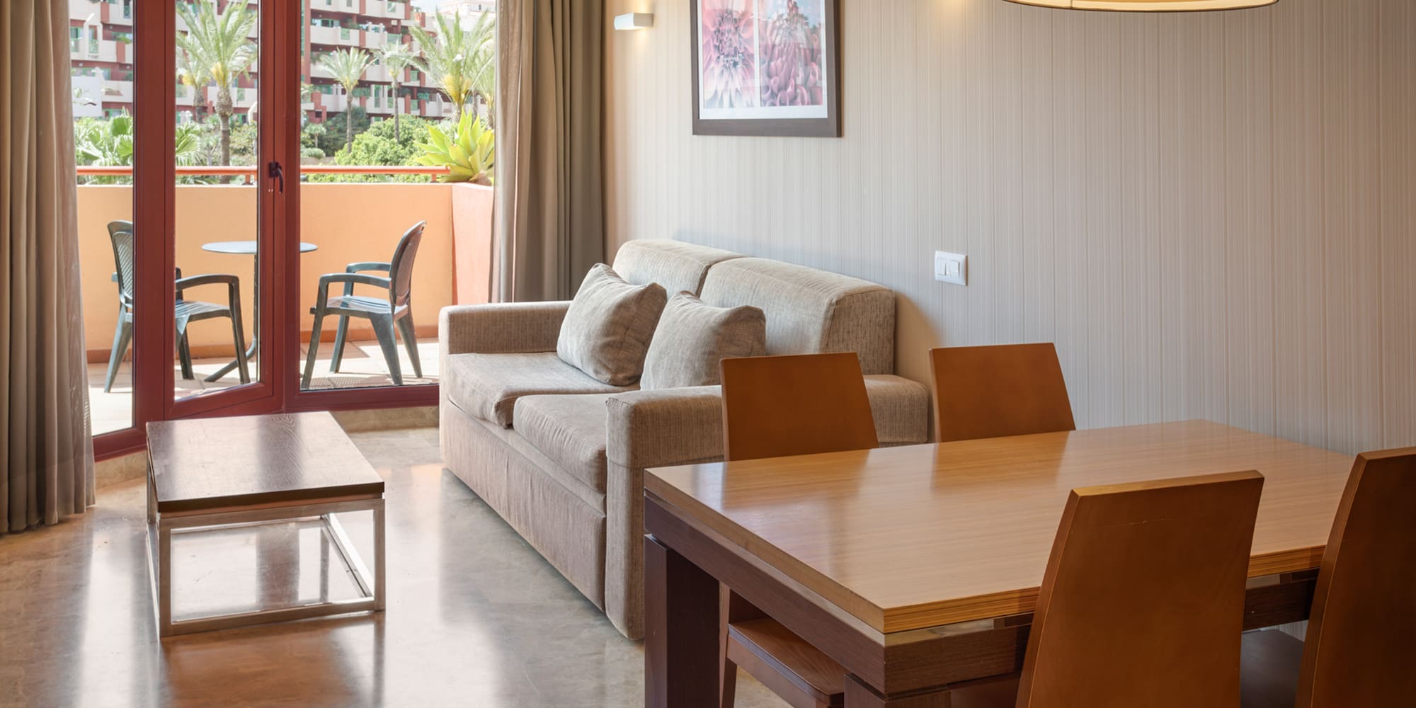 Hotel suite with living, dining areas, and a balcony overlooking a resort complex.