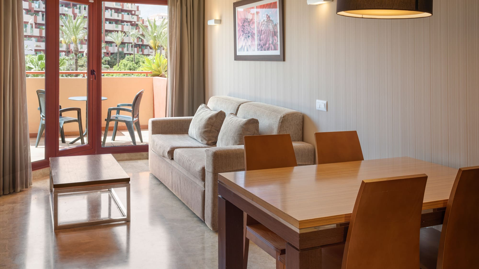 Hotel suite with living, dining areas, and a balcony overlooking a resort complex.