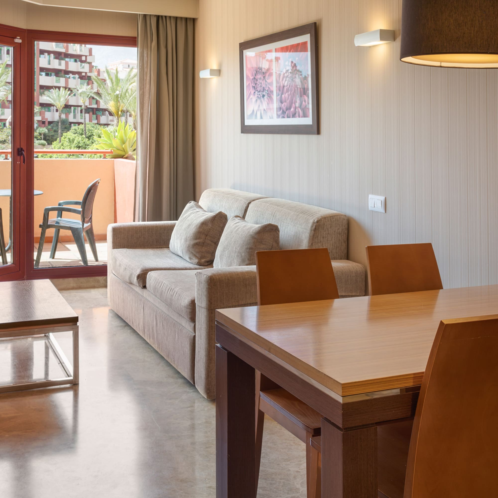 Hotel suite with living, dining areas, and a balcony overlooking a resort complex.