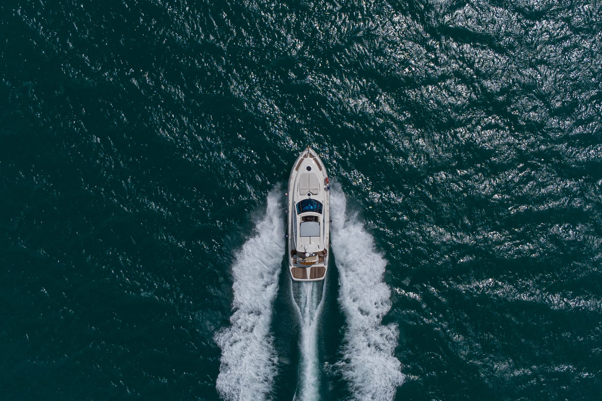Yate blanco navegando rápido en mar azul oscuro, dejando una estela espumosa.