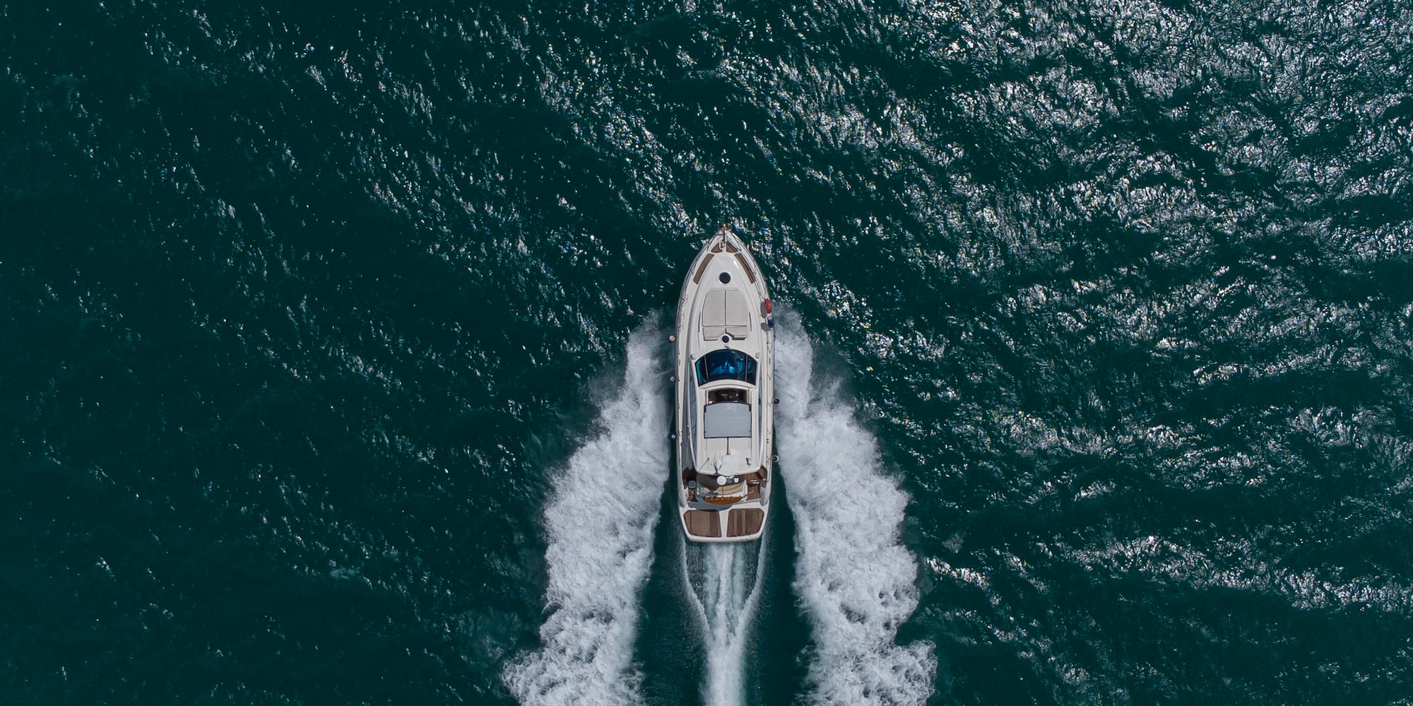 Aerial view of a white motor yacht creating a wake on dark ocean water.