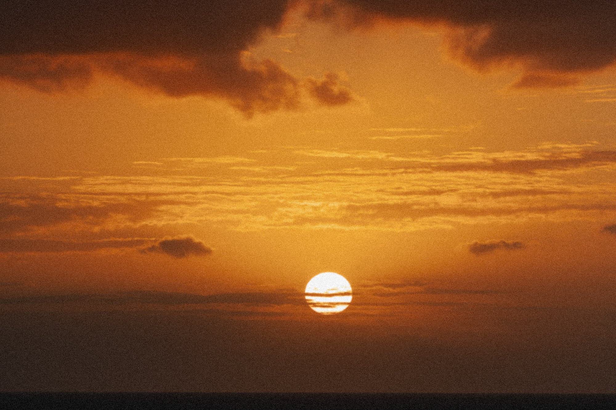 Atardecer naranja sobre el mar, sol poniente y nubes oscuras en el cielo.