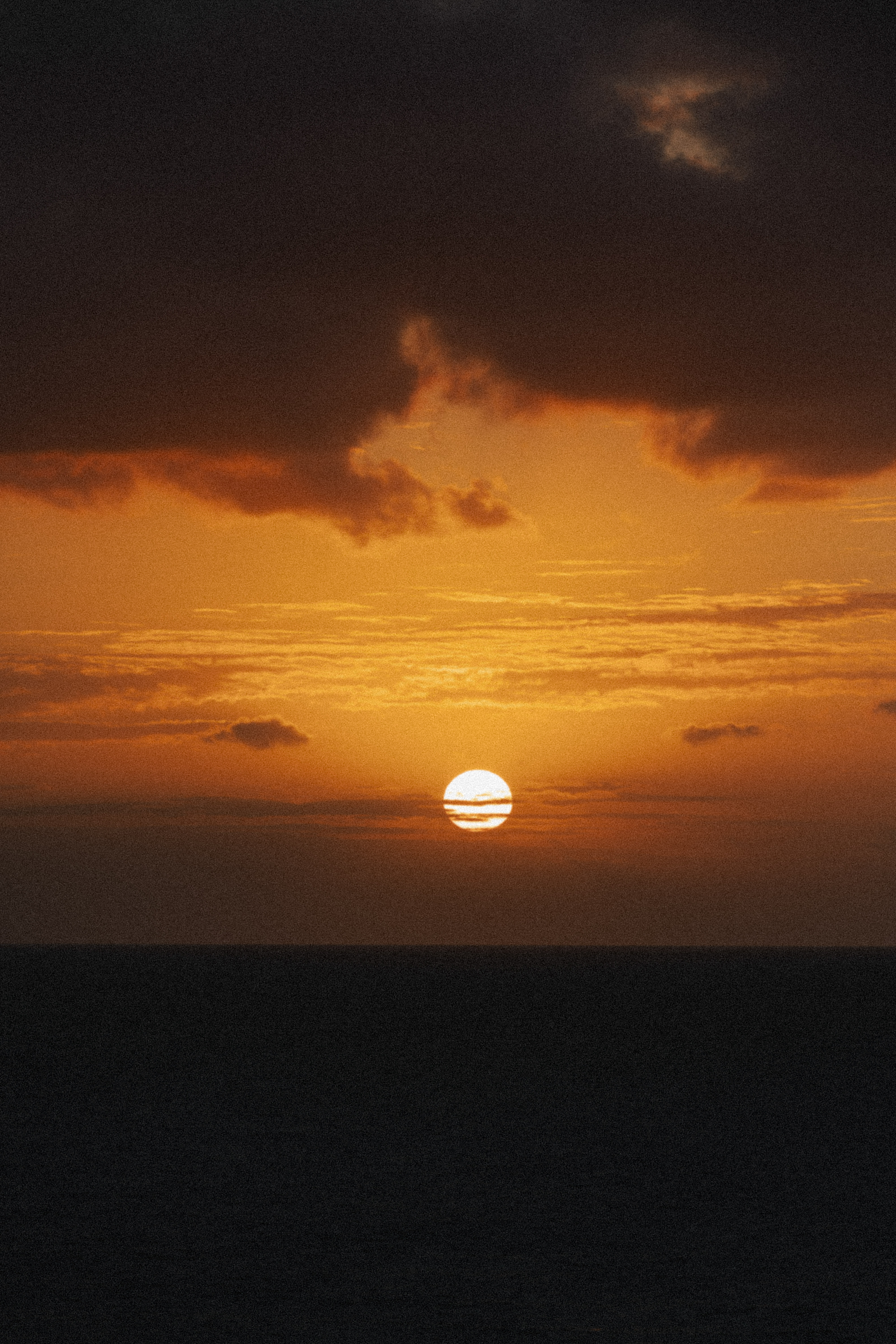 Atardecer naranja sobre el mar, sol poniente y nubes oscuras en el cielo.