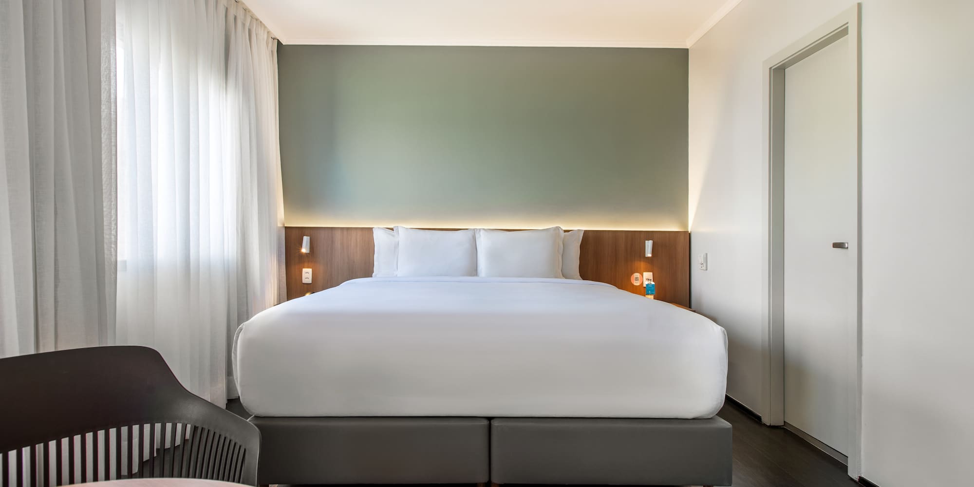 Modern hotel room with king bed, green accent wall, and wood floor.
