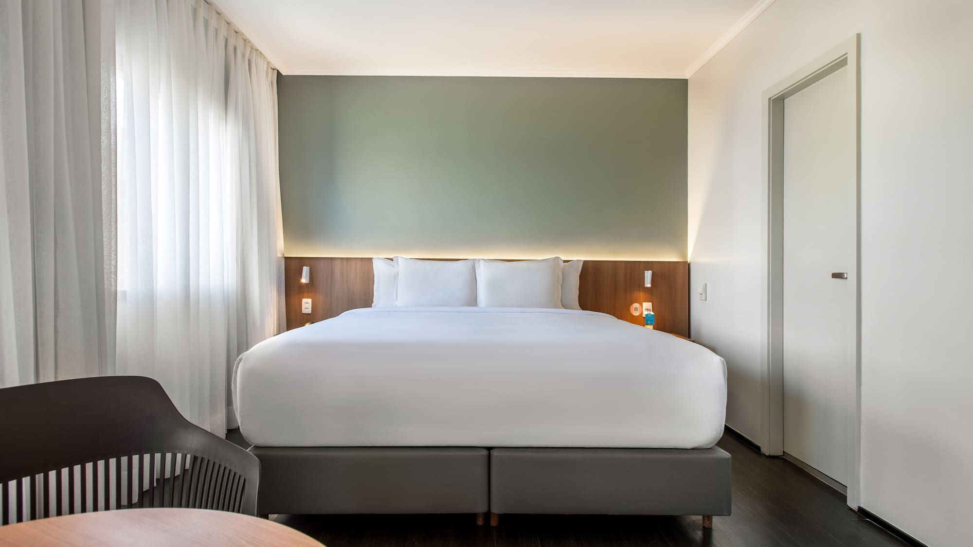 Modern hotel room with king bed, green accent wall, and wood floor.