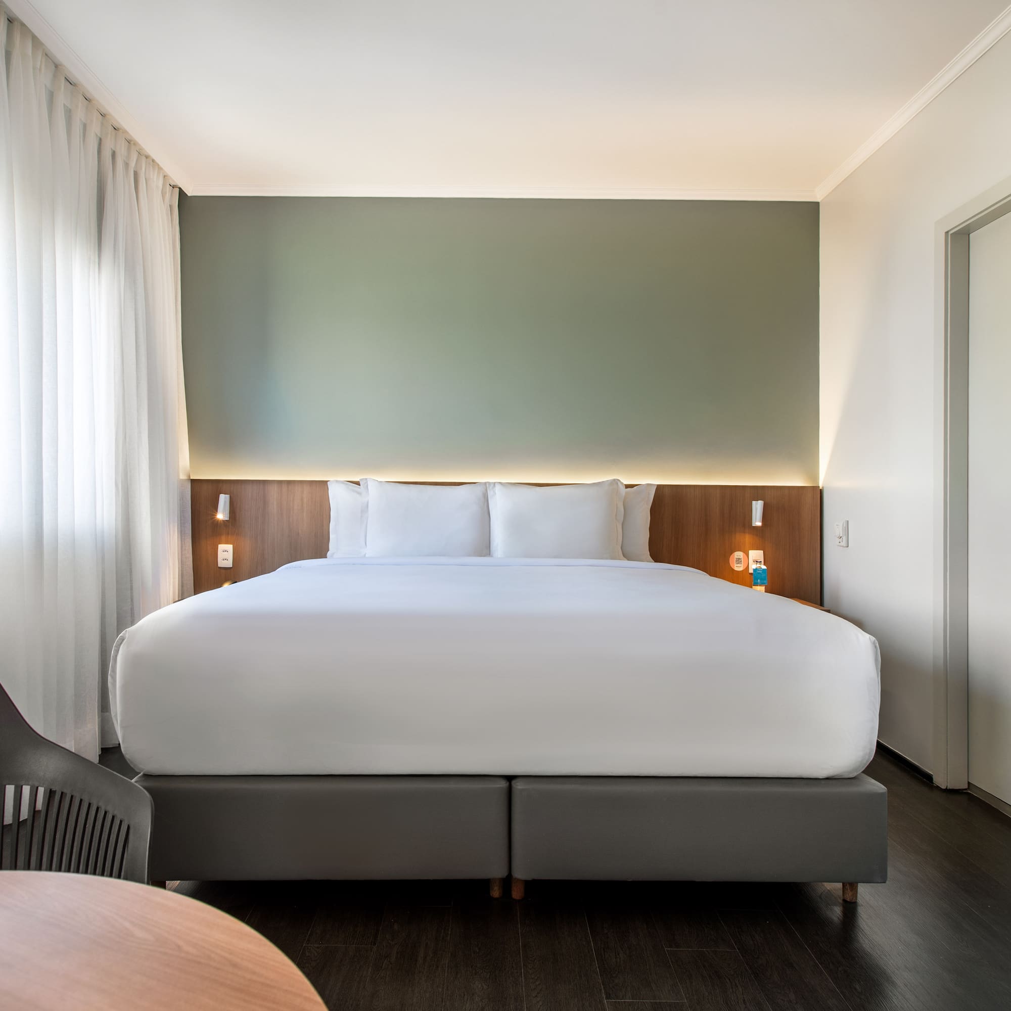 Modern hotel room with king bed, green accent wall, and wood floor.