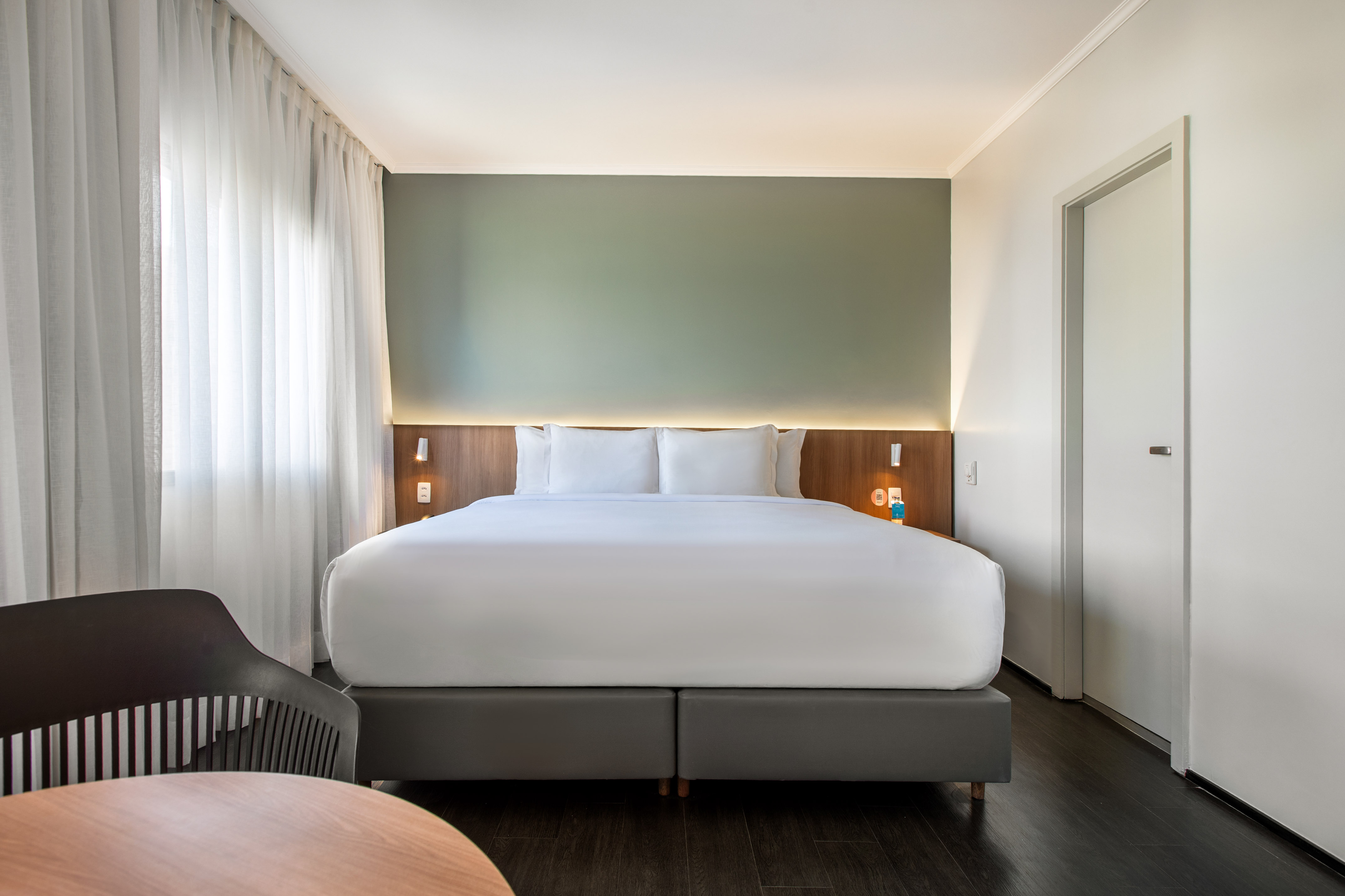 Modern hotel room with king bed, green accent wall, and wood floor.