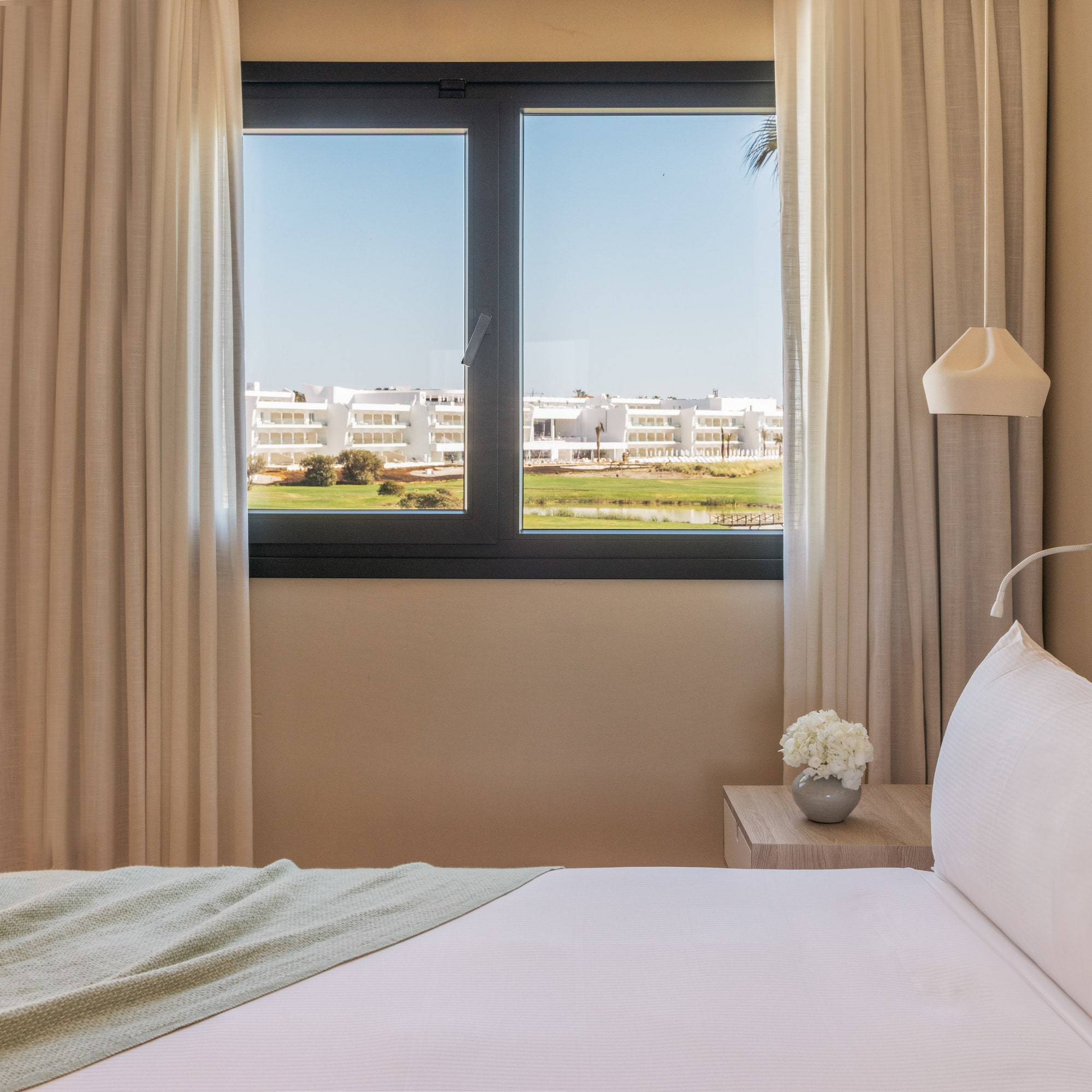 Modern hotel bedroom with golf course view, white bed.