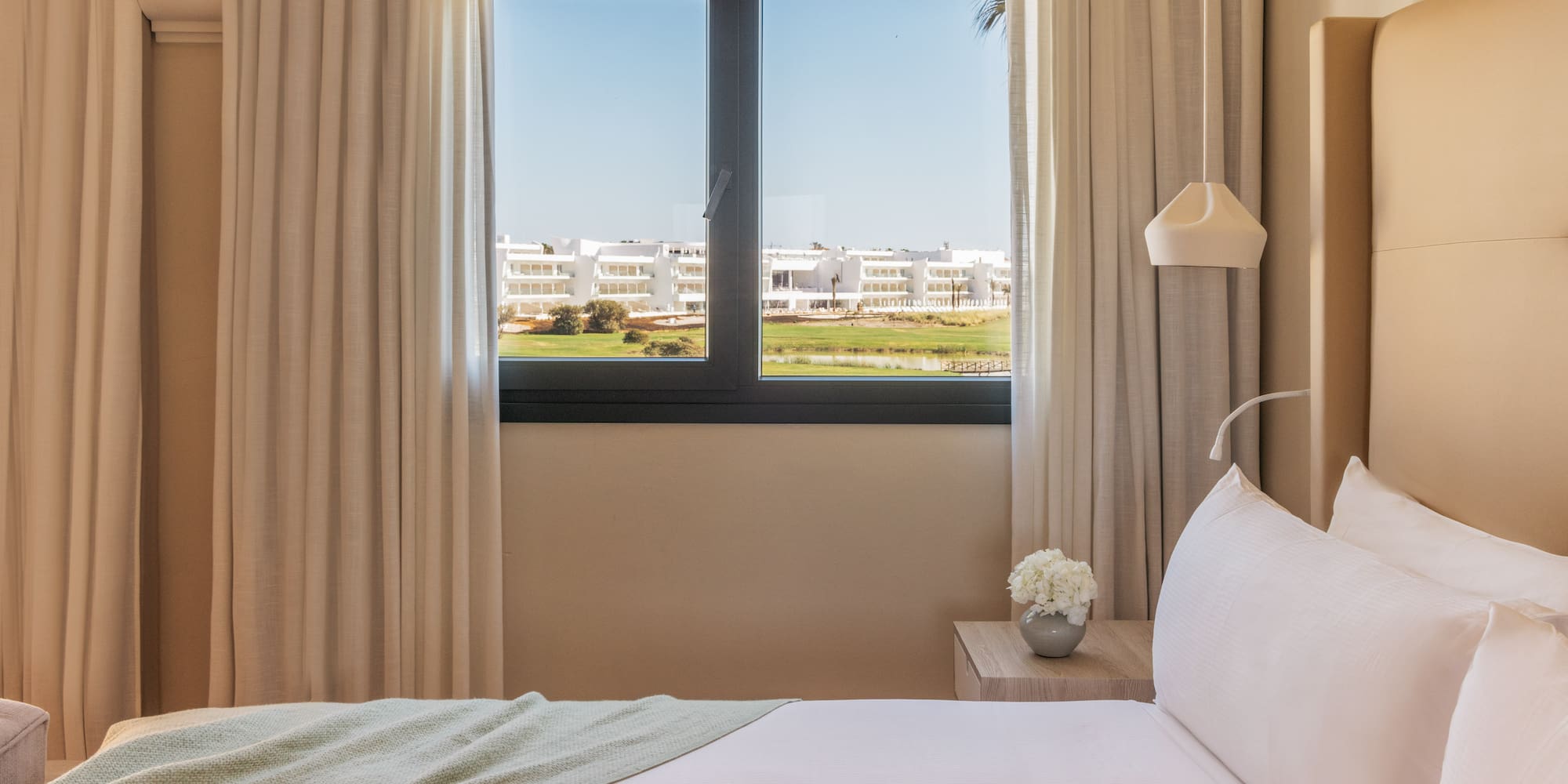 Modern hotel bedroom with golf course view, white bed.