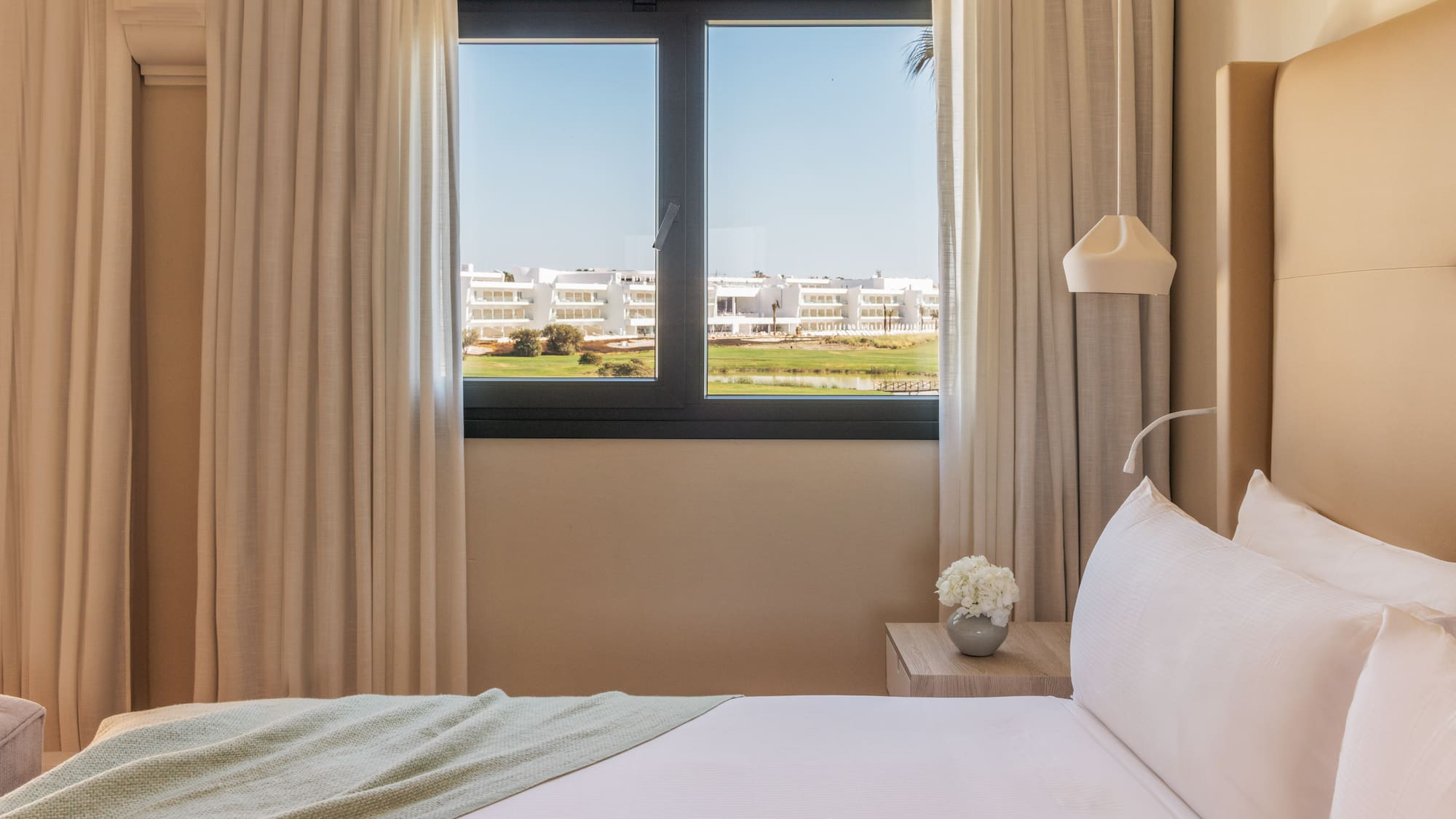 Modern hotel bedroom with golf course view, white bed.