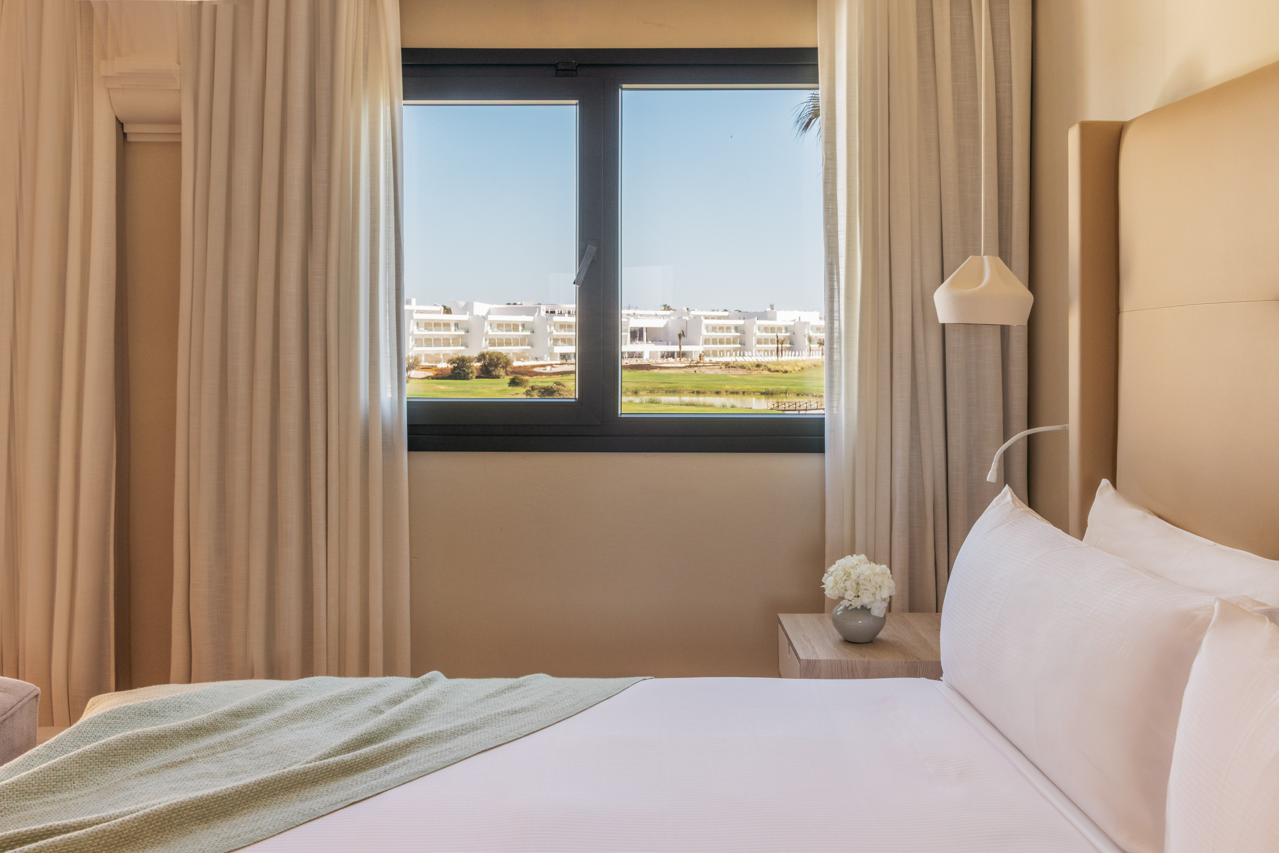 Modern hotel bedroom with golf course view, white bed.