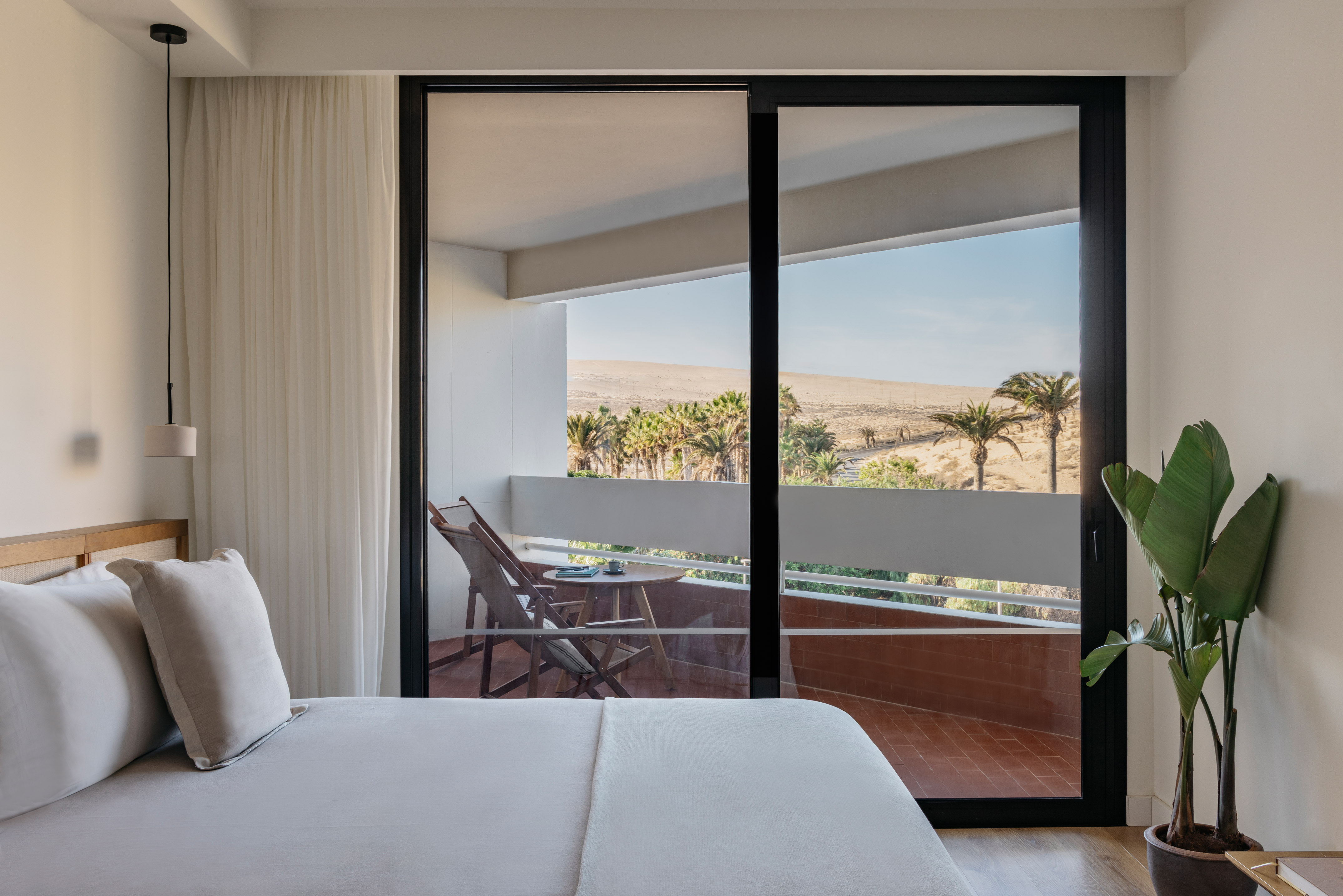 Hotel room with private balcony, desert view, palm trees, and modern bed.
