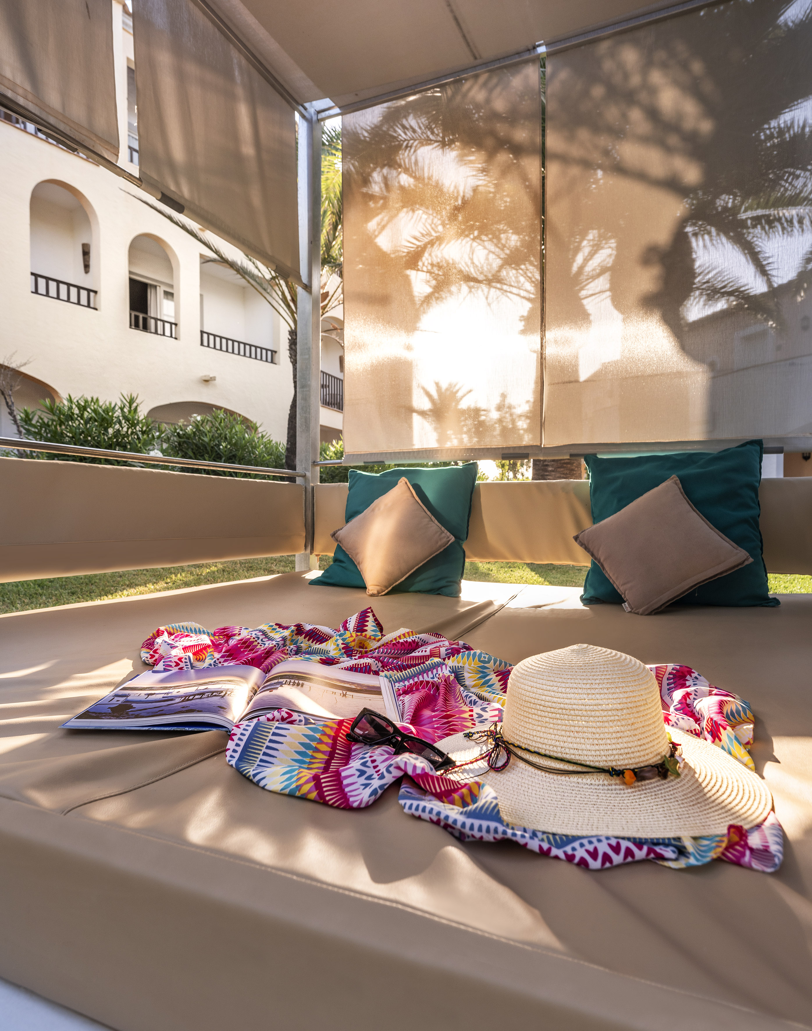 Sunny resort cabana with colorful towel, magazine, straw hat, and sunglasses.