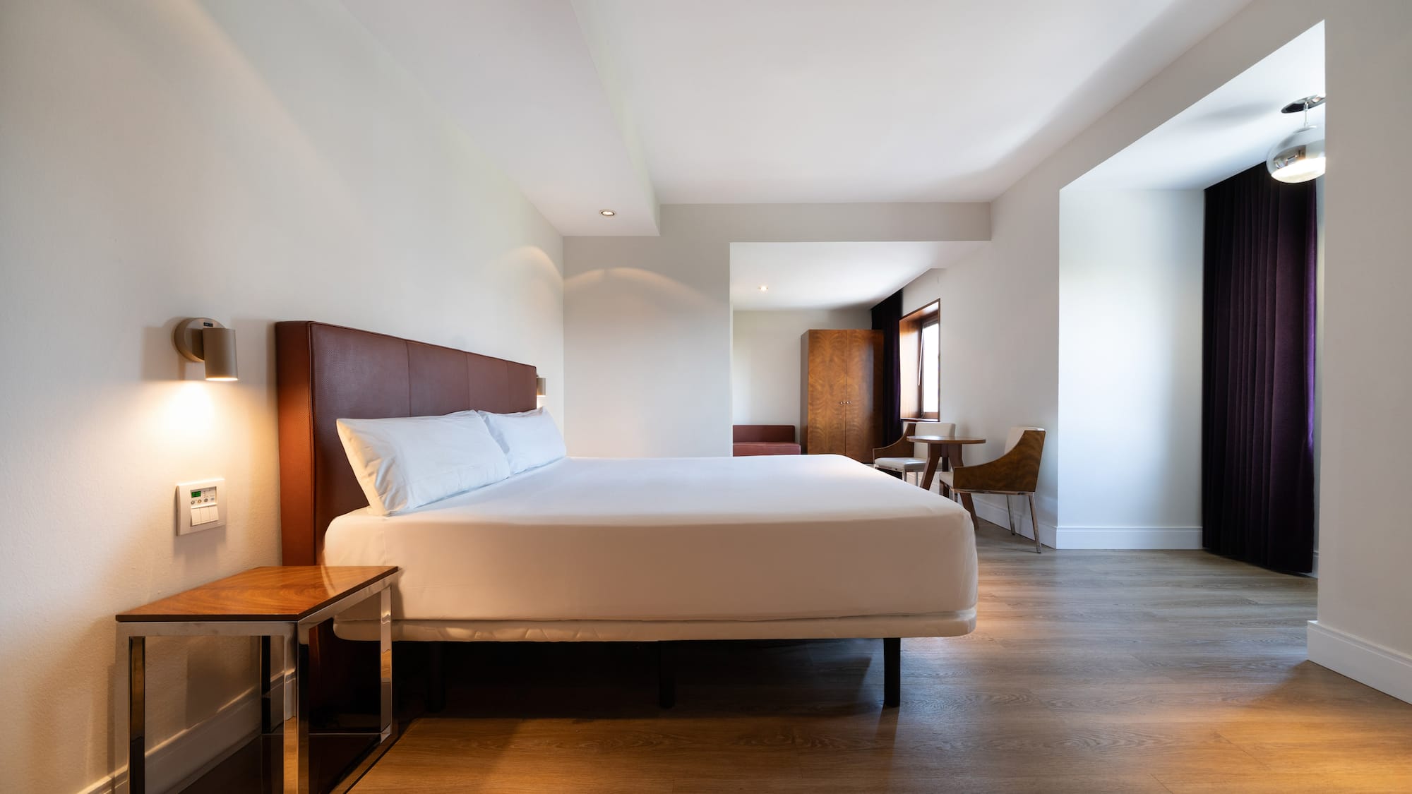 Modern hotel room with king bed, wooden floor, and adjacent sitting area.