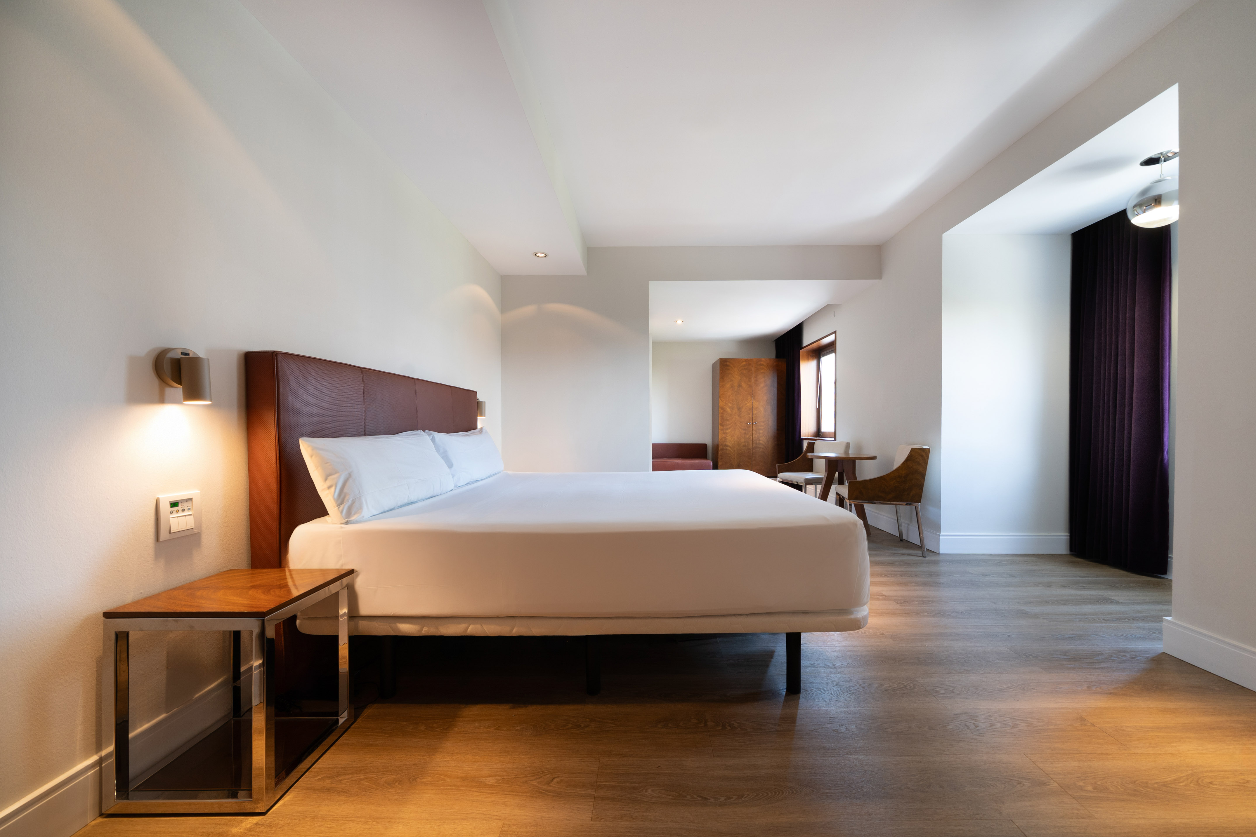 Modern hotel room with king bed, wooden floor, and adjacent sitting area.