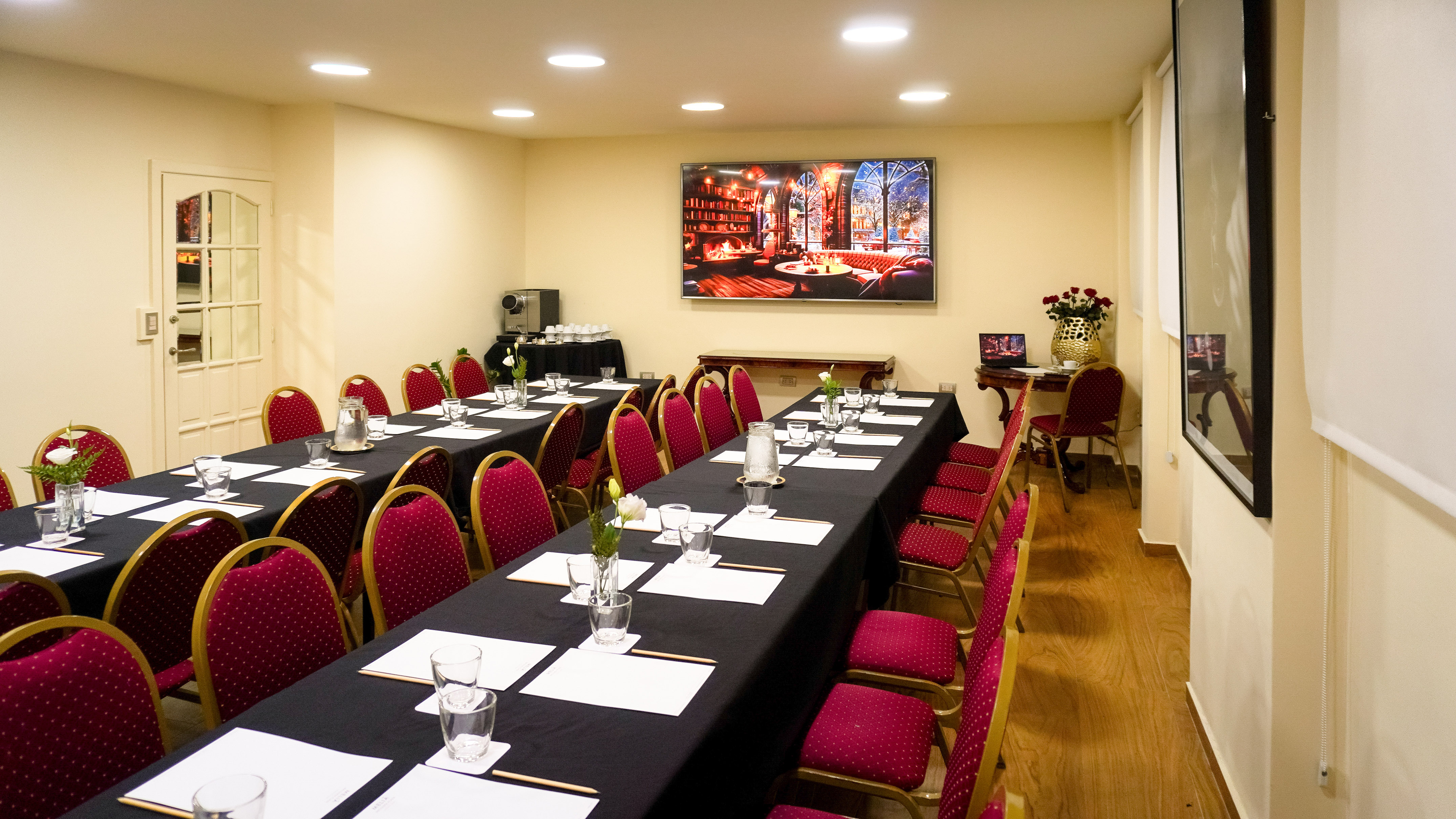 Professional conference room with long tables, red chairs, and a large screen display.