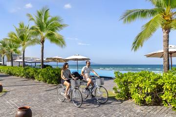 a man and woman riding bicycles on a sidewalk by the ocean