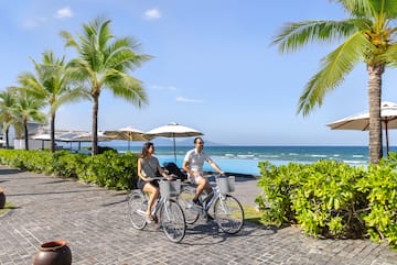 a man and woman riding bicycles on a sidewalk by the ocean