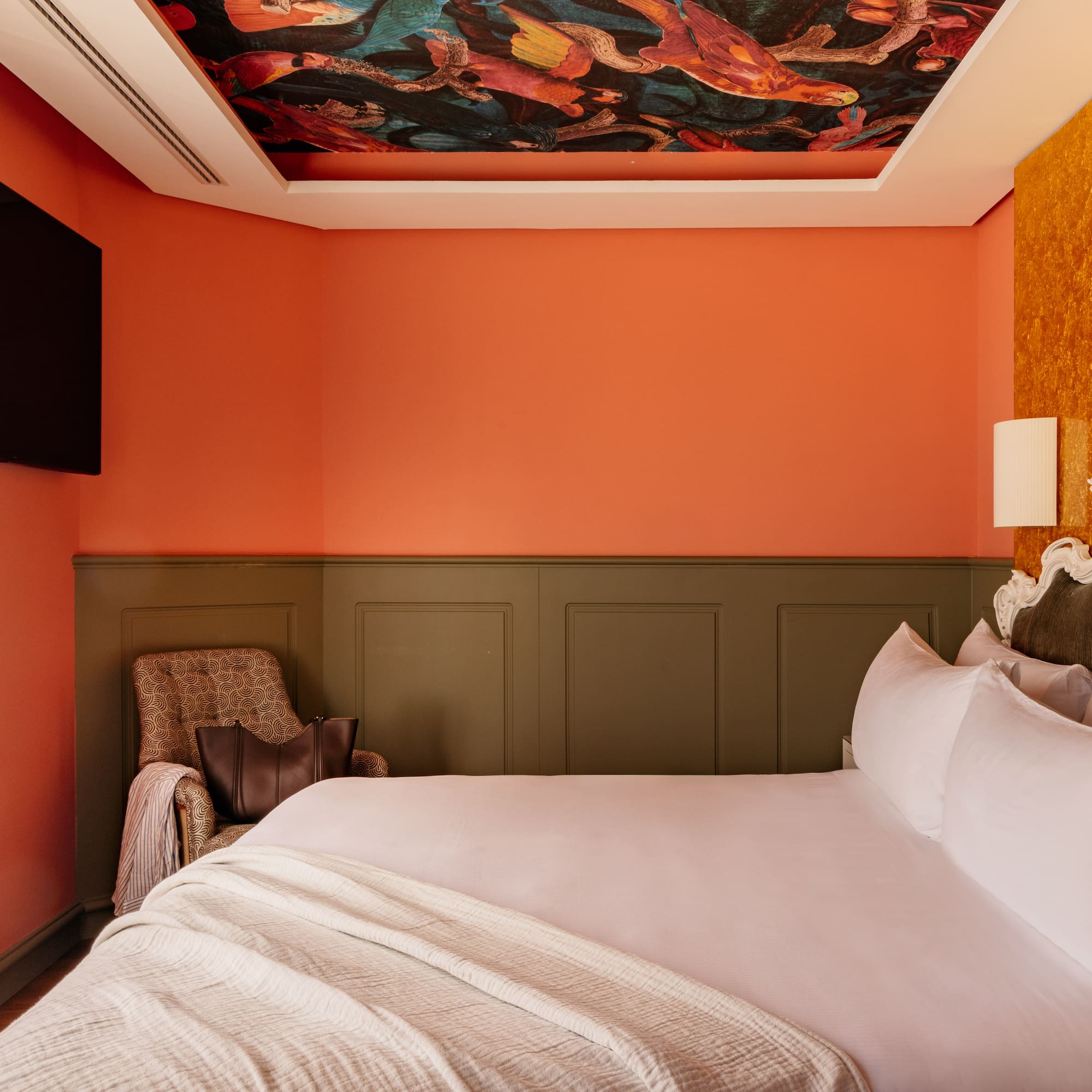 Habitación boutique con techo artístico, cama king, paredes naranja y oro.