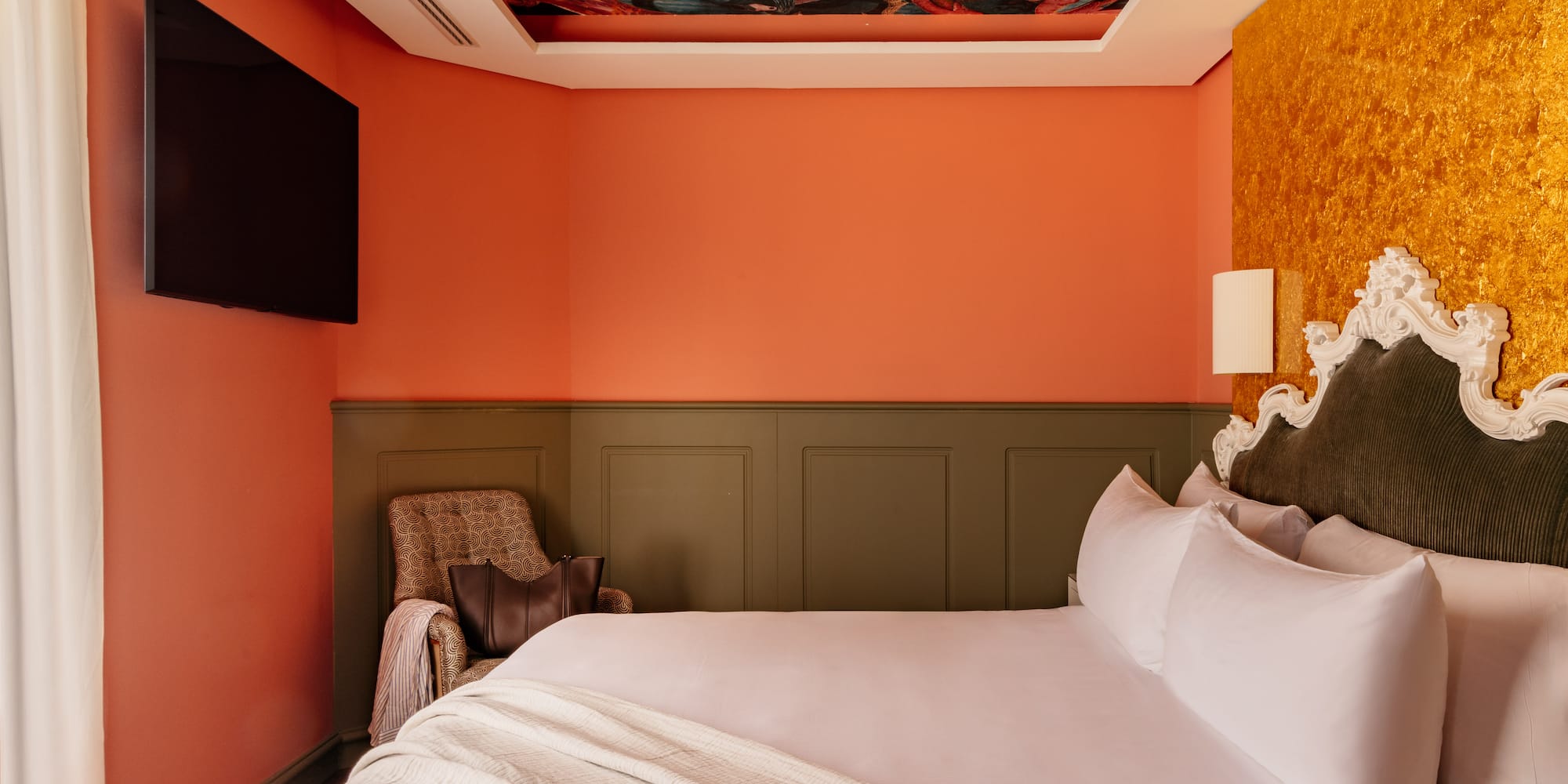 Habitación boutique con techo artístico, cama king, paredes naranja y oro.