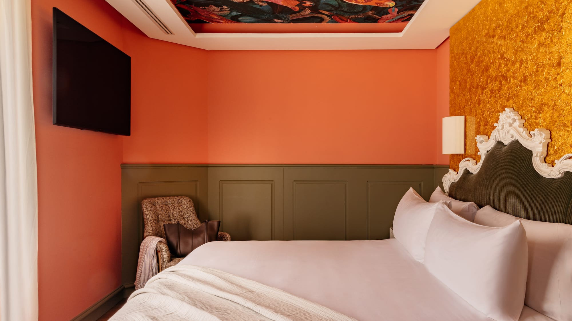 Habitación boutique con techo artístico, cama king, paredes naranja y oro.