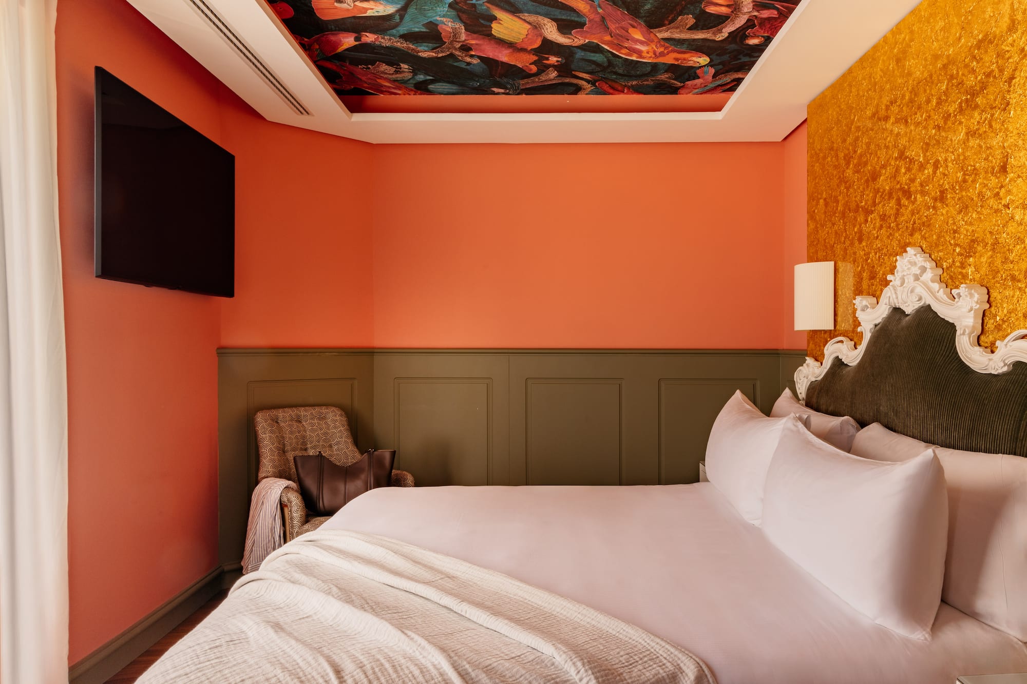 Habitación boutique con techo artístico, cama king, paredes naranja y oro.