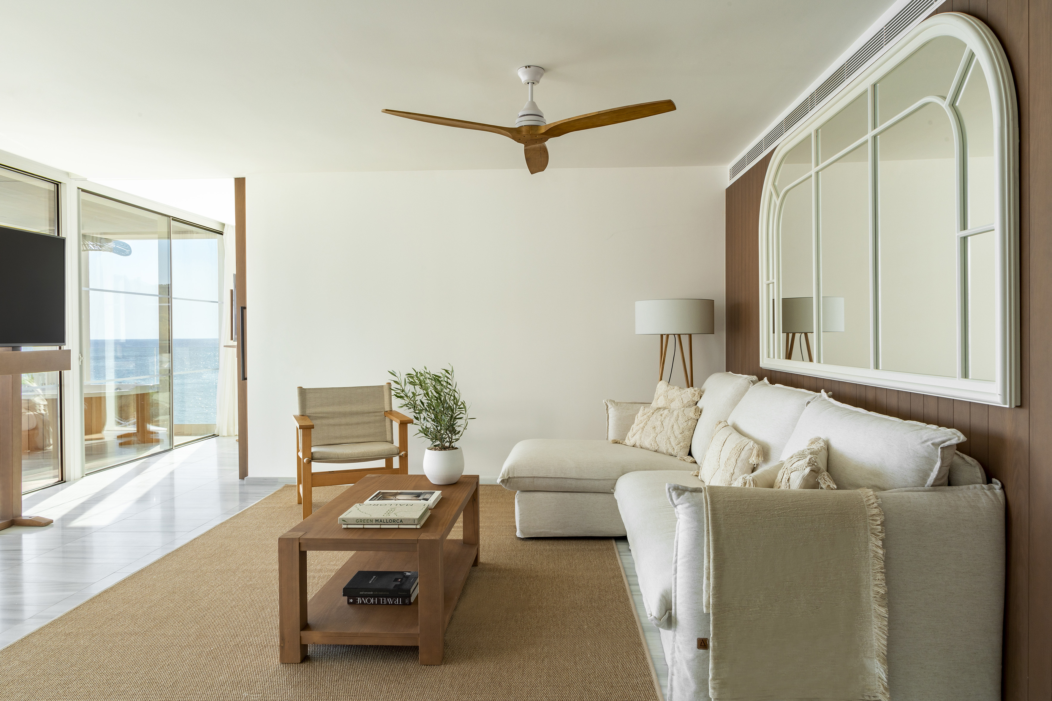 Modern coastal living room with white sectional, wooden fan, and ocean view.