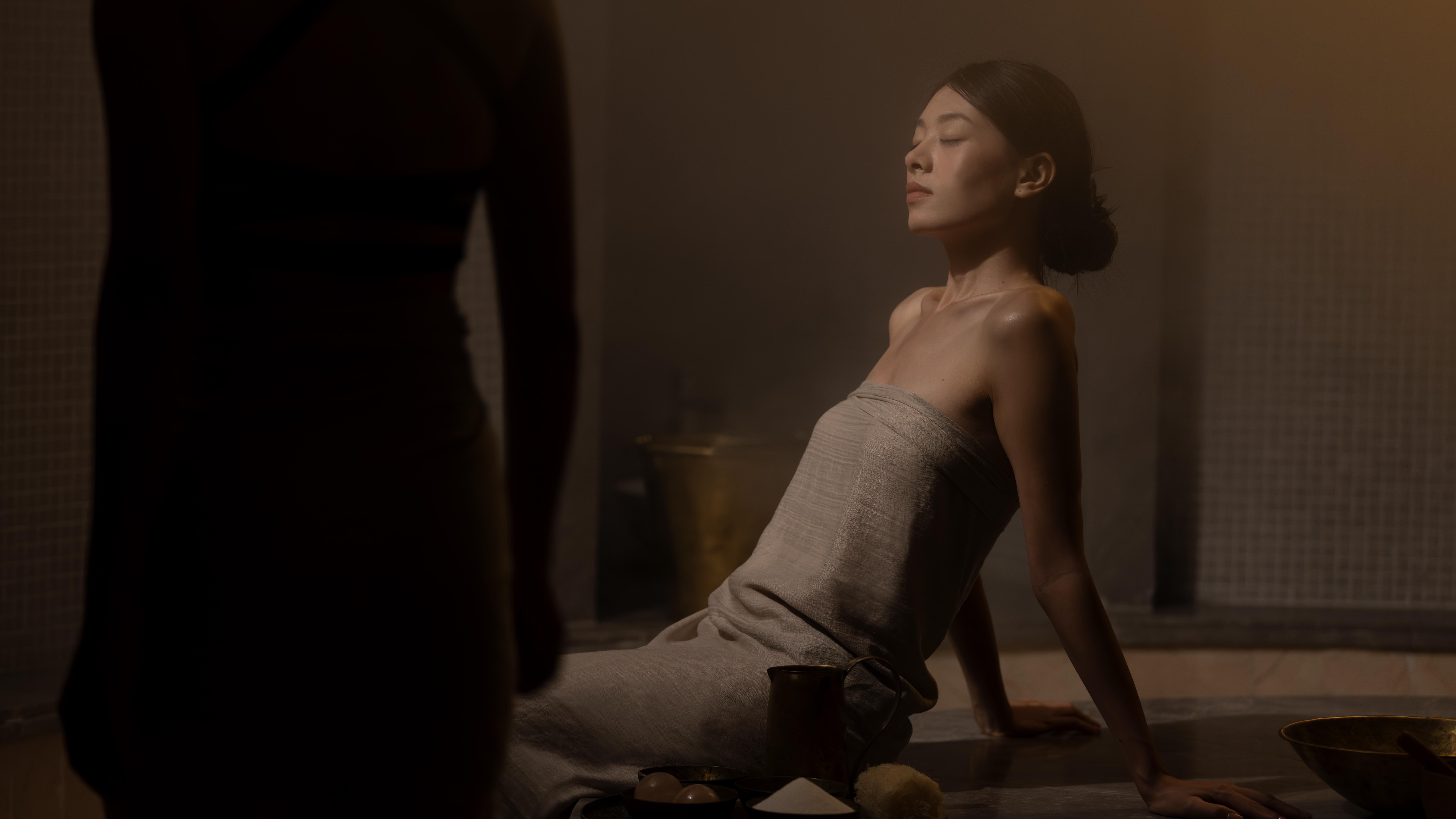 Woman relaxing at a dimly lit spa, eyes closed, with natural treatment ingredients.