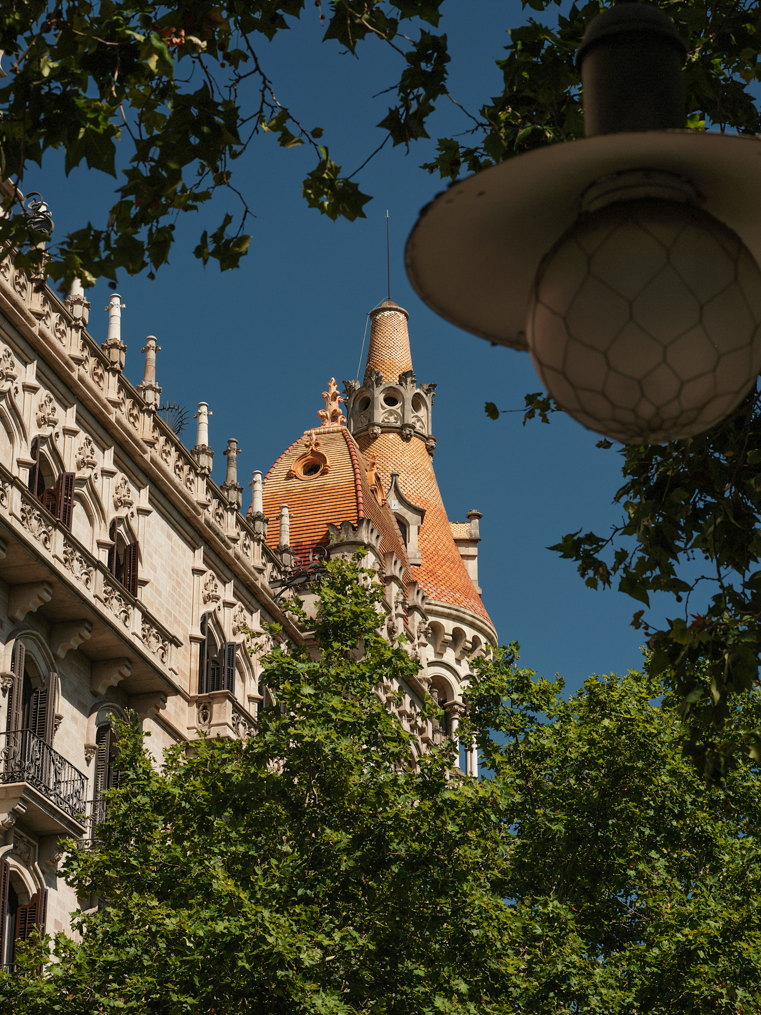 Historic Barcelona building with an ornate tiled turret through green trees.