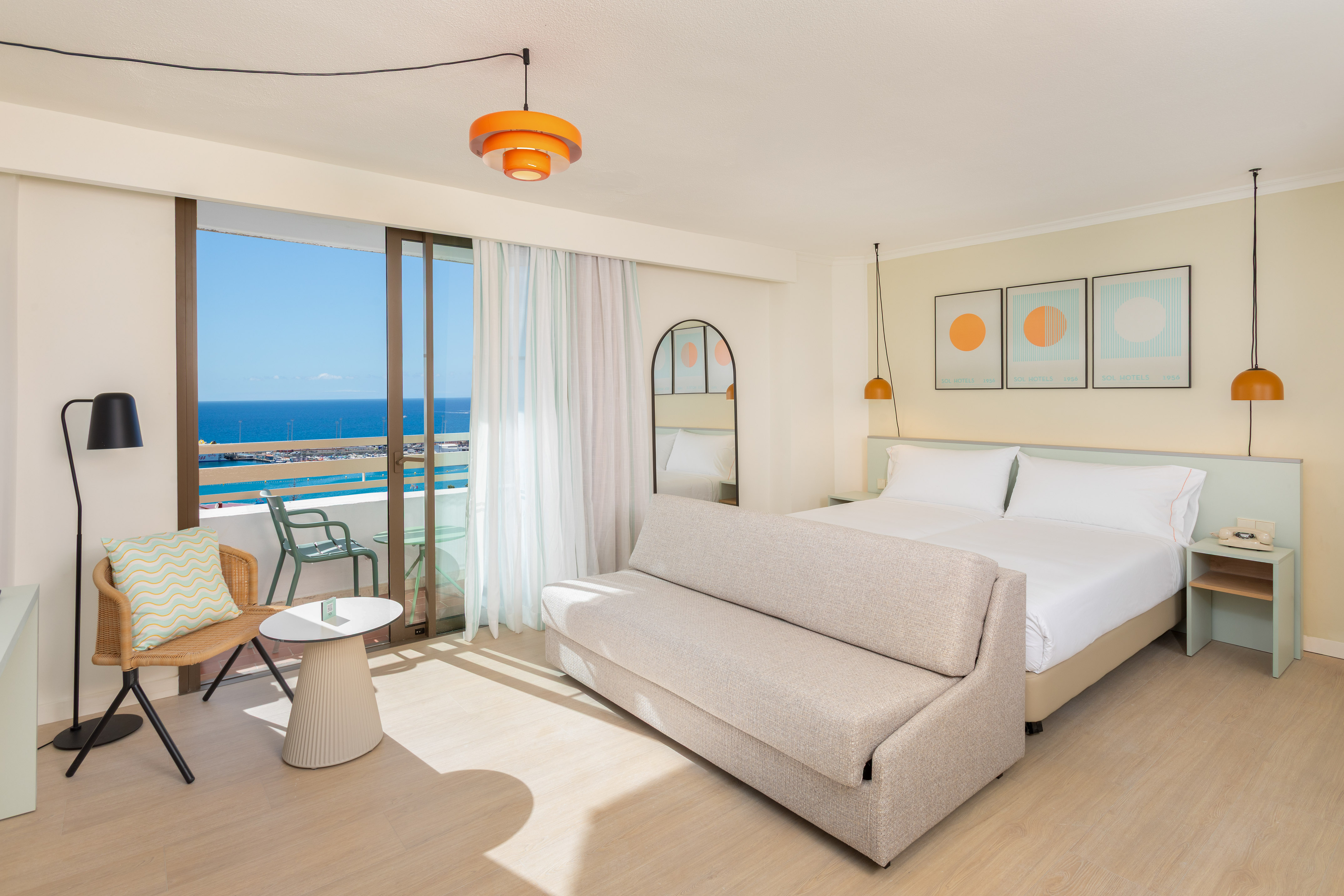 Modern hotel room with sea view balcony, bed, and sofa bed.