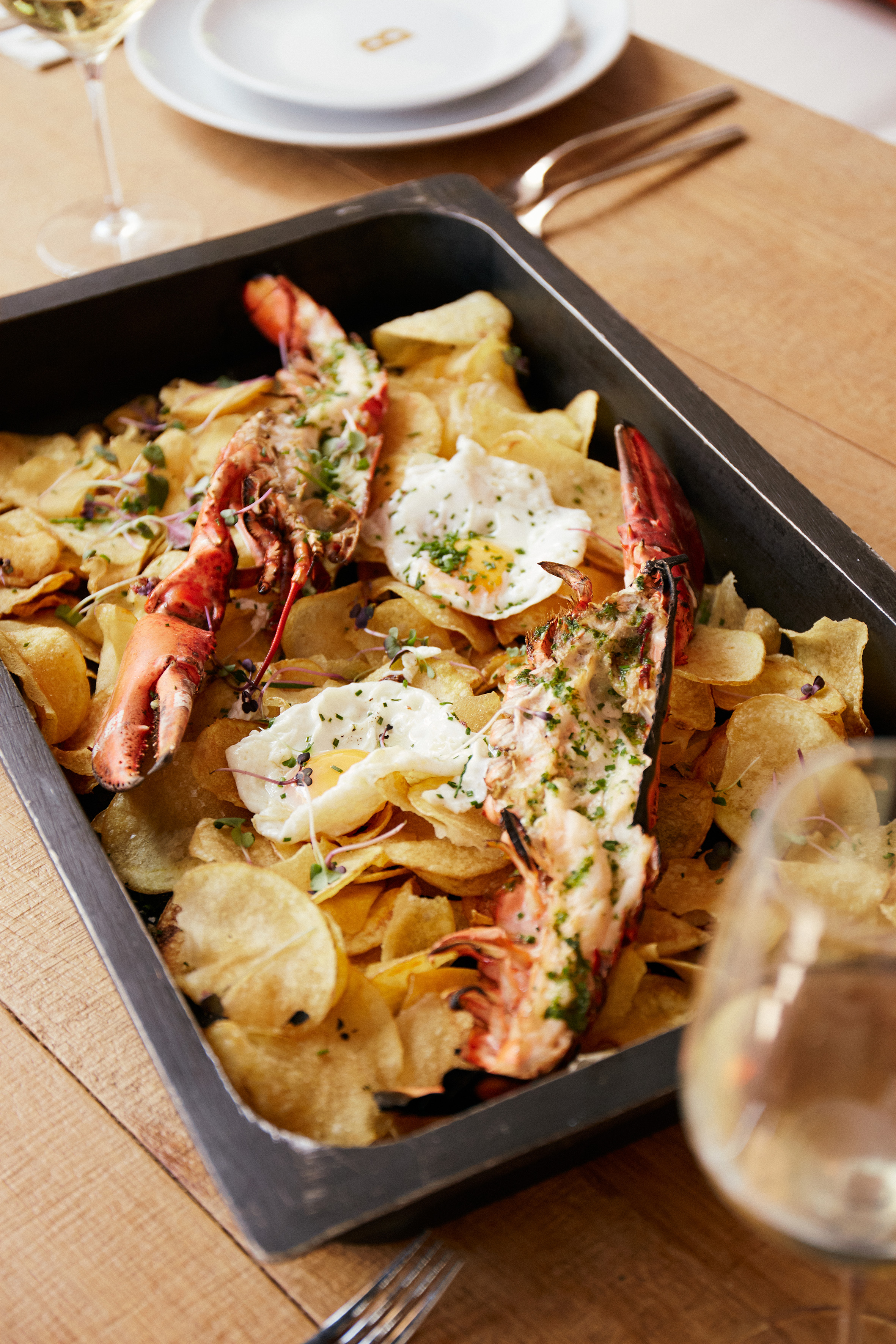 Gourmet grilled lobster, crispy chips, and fried eggs in a serving tray.