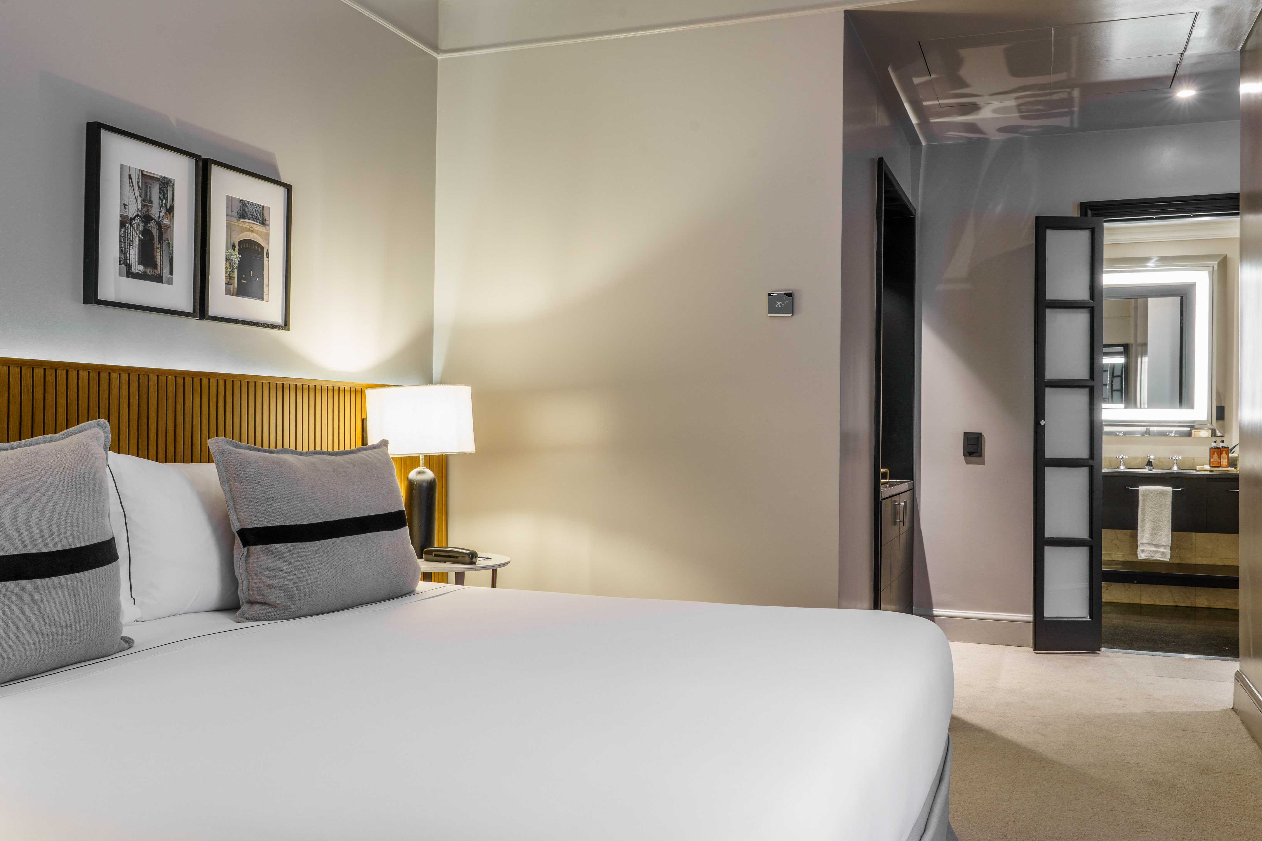 Modern hotel bedroom with king bed, wood headboard, and ensuite bathroom.