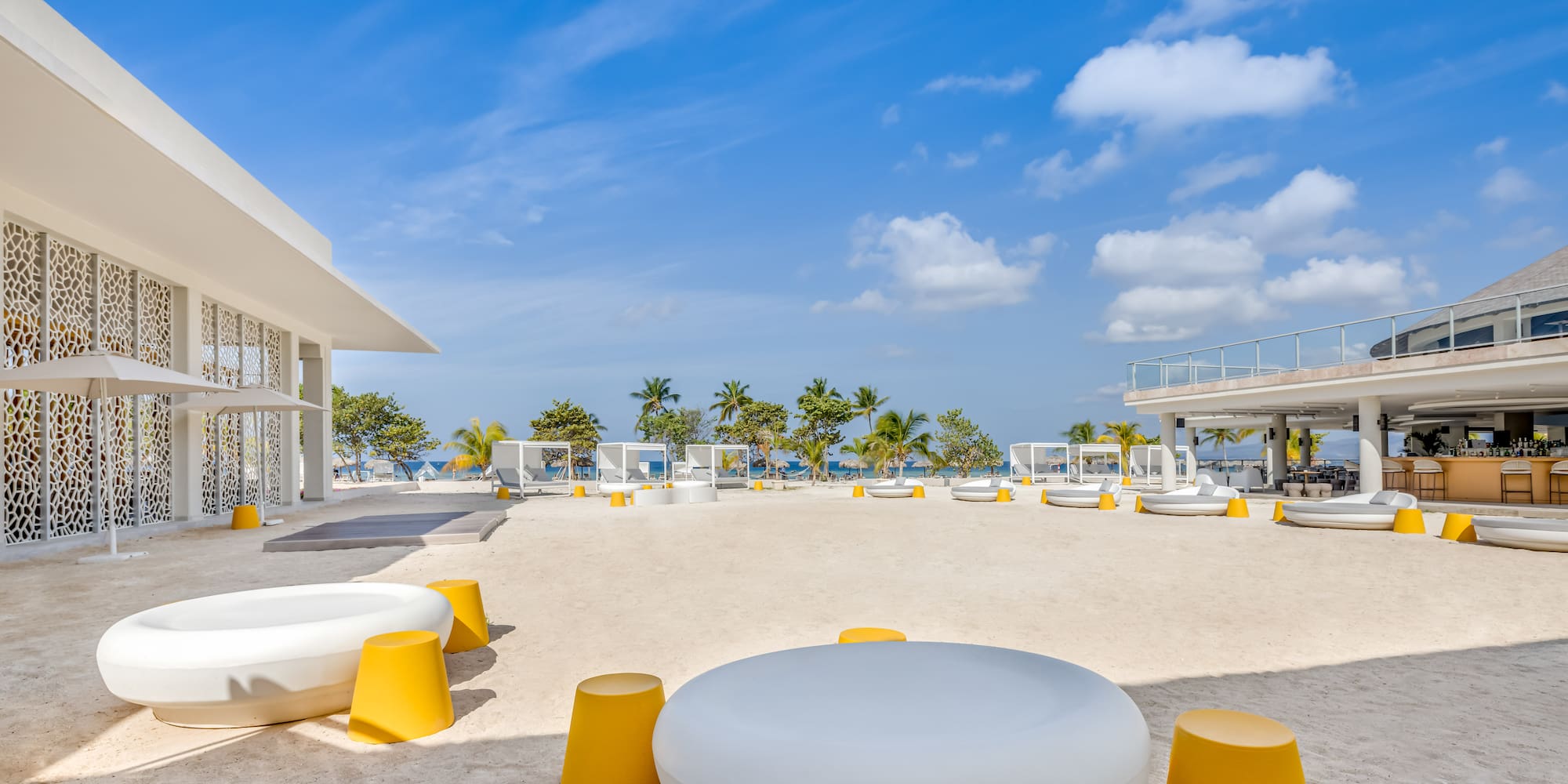 a white and yellow chairs on a sandy area with trees and blue sky