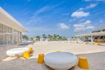 a white and yellow chairs on a sandy area with trees and blue sky