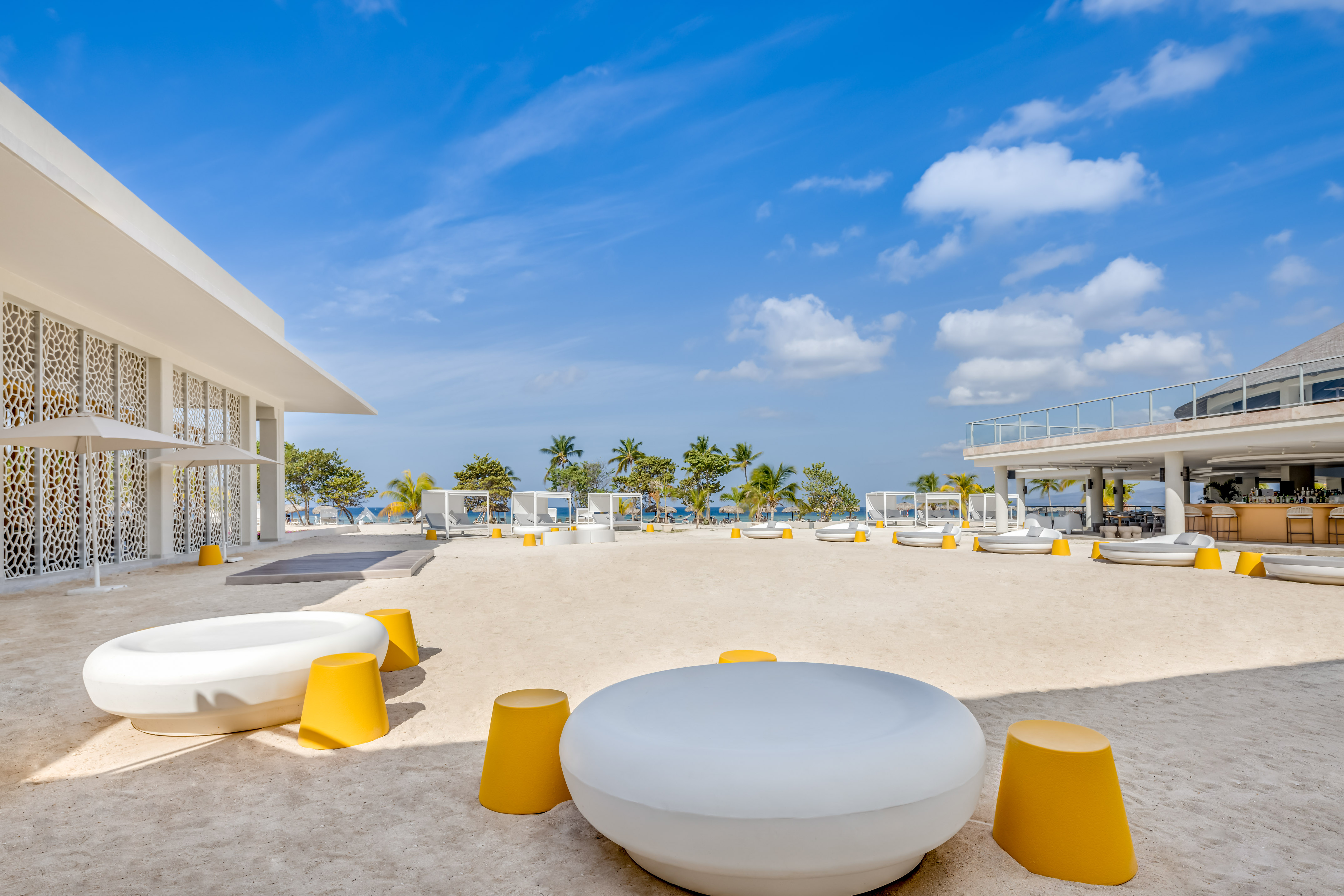 a white and yellow chairs on a sandy area with trees and blue sky