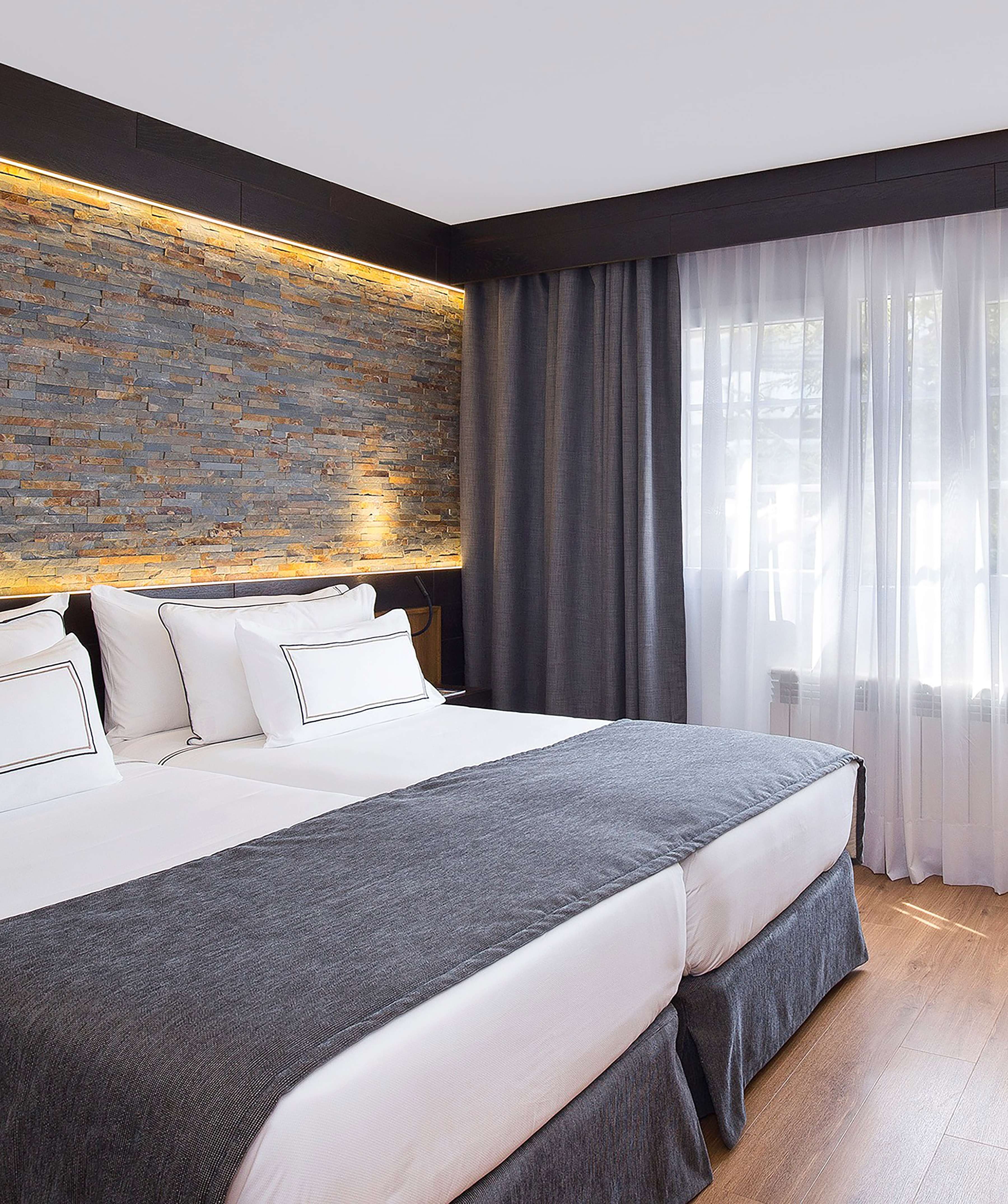 Twin beds in modern hotel room with stone accent wall and warm lighting.