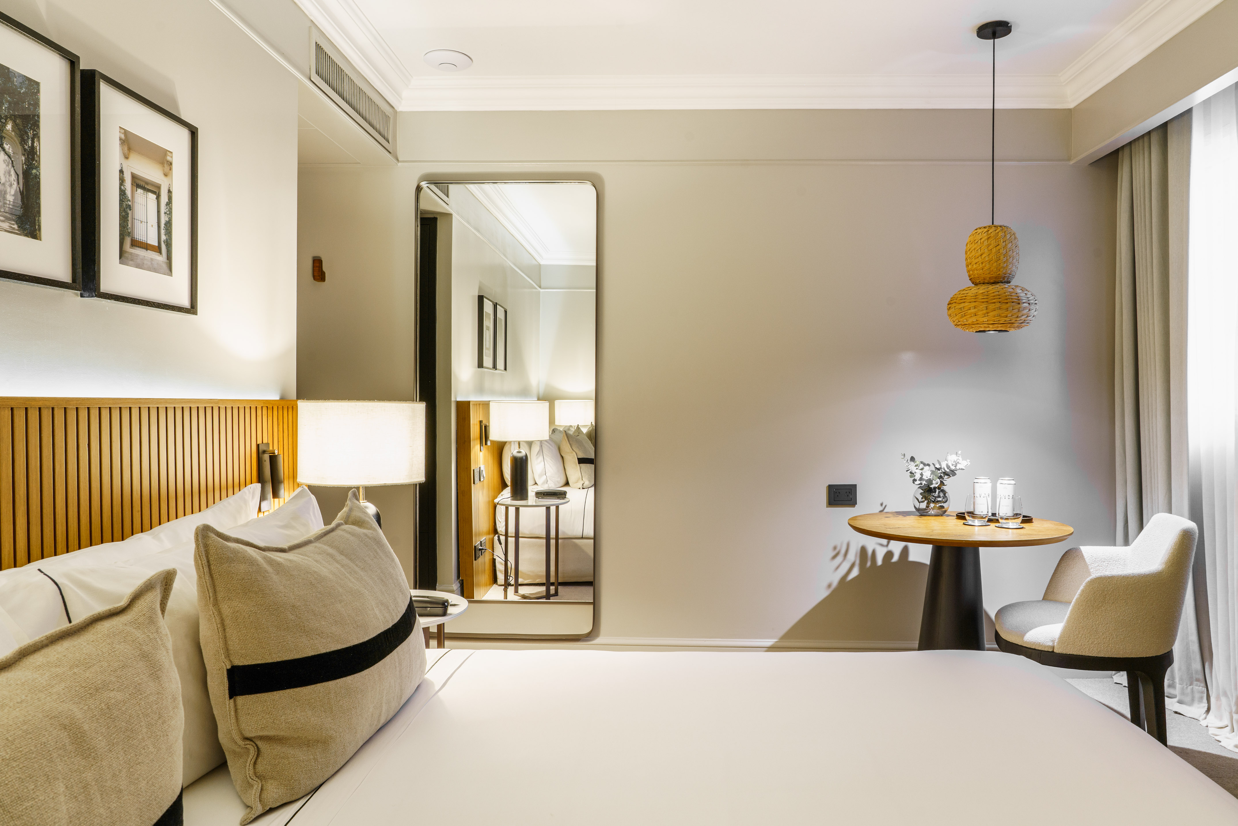 Modern hotel bedroom with cozy bed, wooden headboard, mirror, and stylish neutral decor.