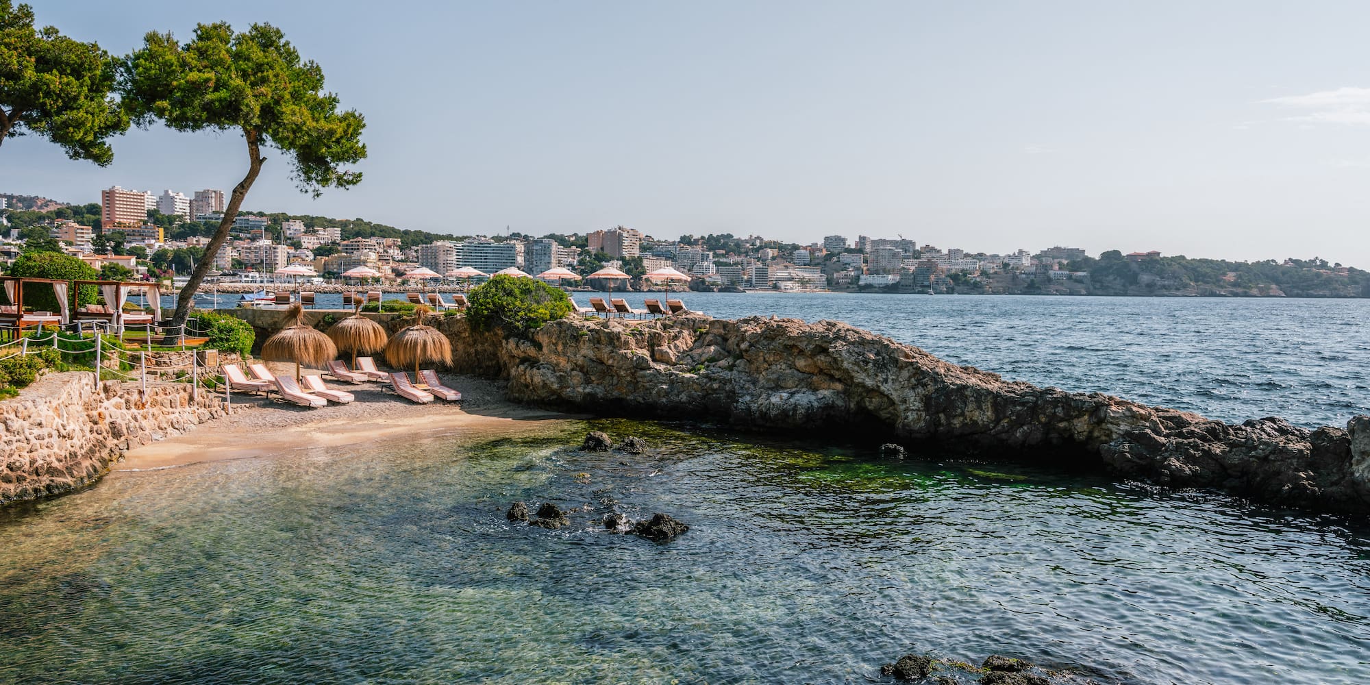 a beach with umbrellas and chairs on a rocky shore.